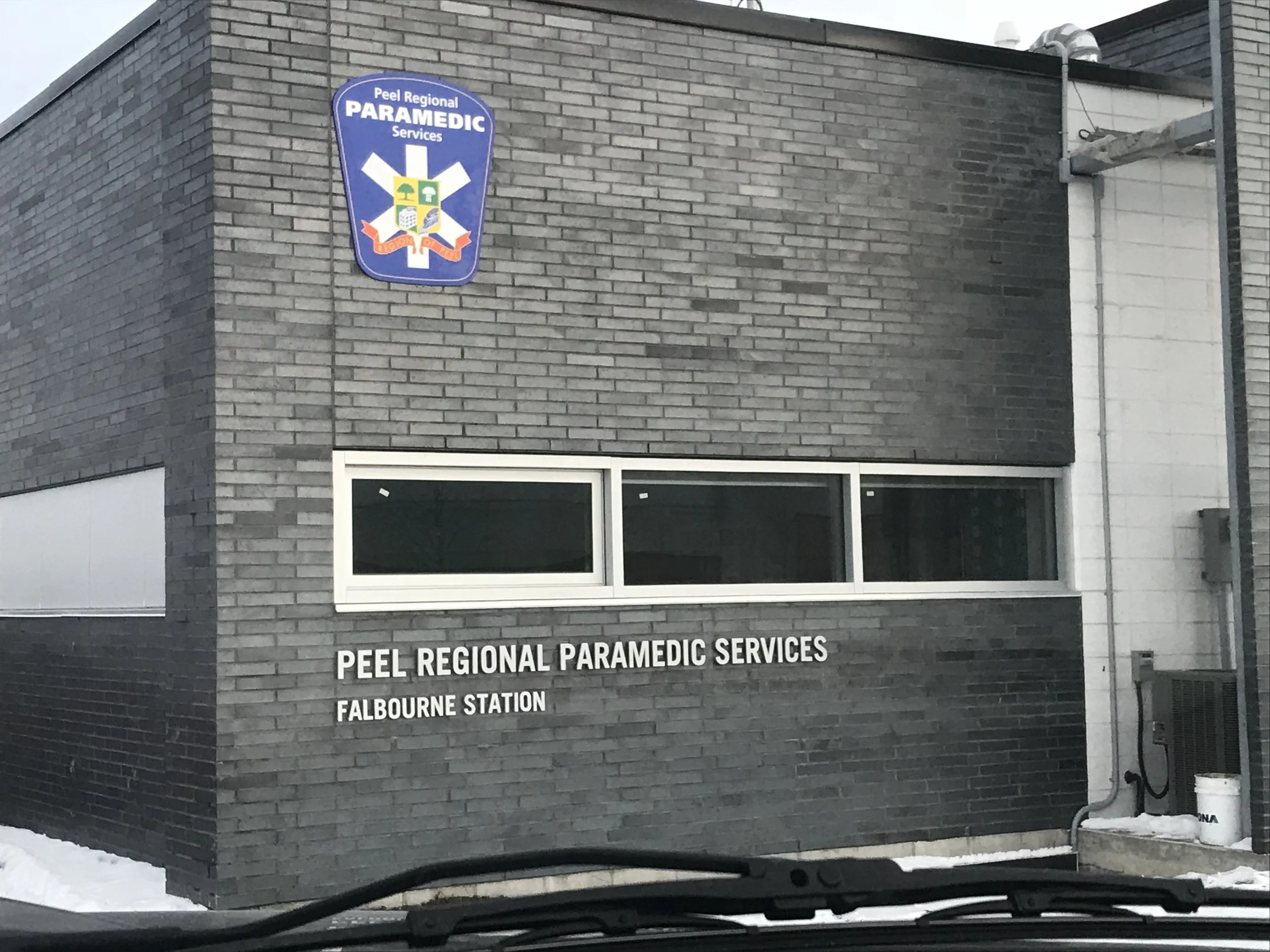 A brick building with a sign that reads 'Peel Regional Paramedic Services, Falbourne Station.' The sign has a blue background with a medical emblem and text.