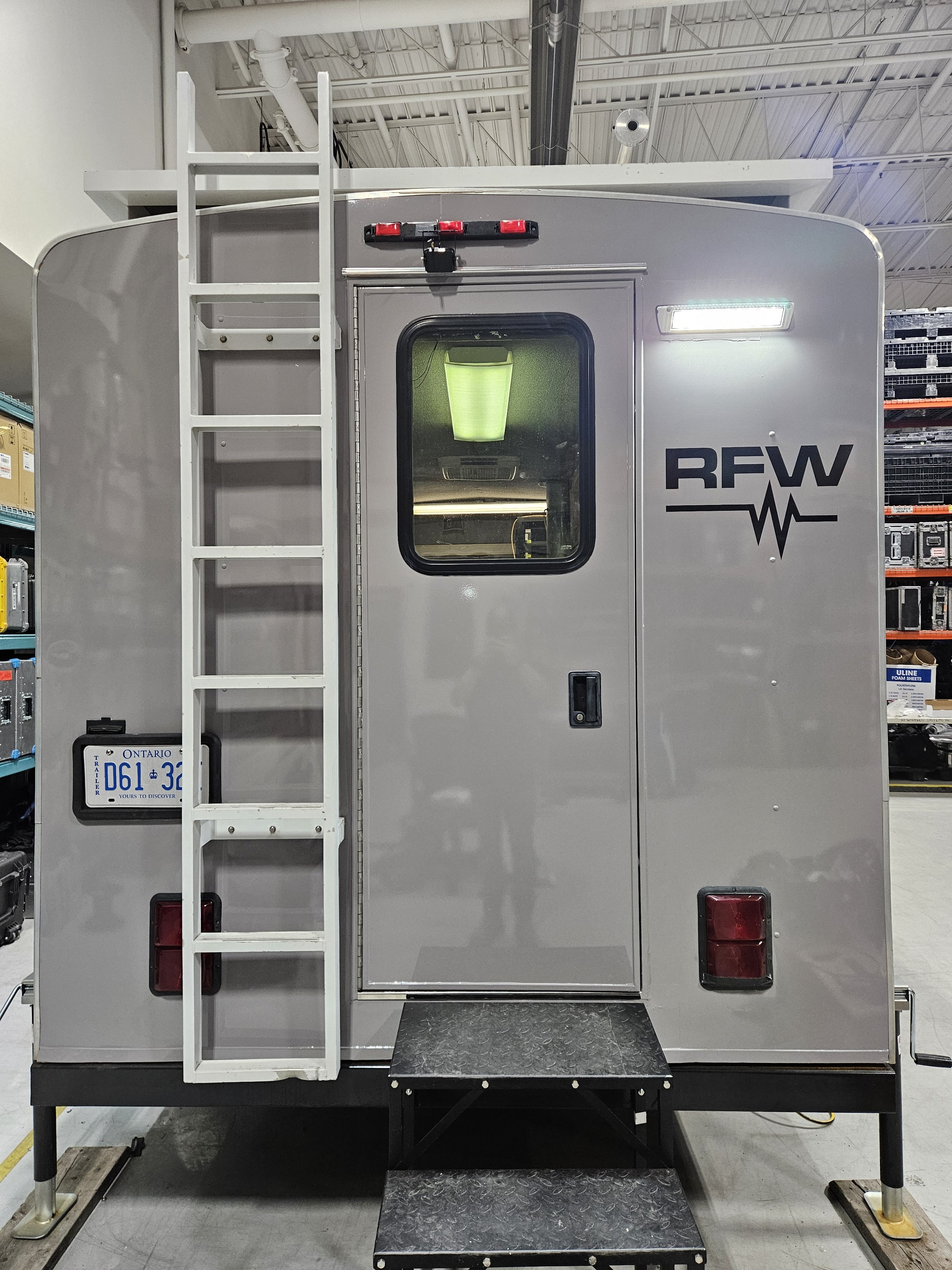 Appearance of an emergency medical services (EMS) vehicle or ambulance with an Ontario license plate, stairs, a ladder on the side, and the letters 