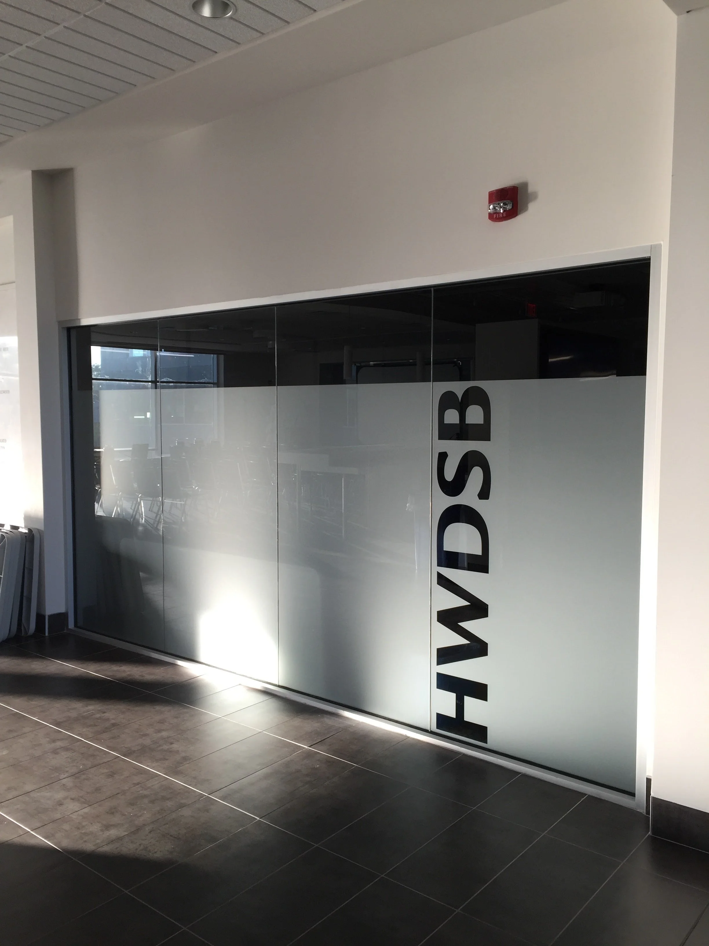 A glass door with the word 'HWD SB' written vertically in black letters, located in an airport or similar public space.