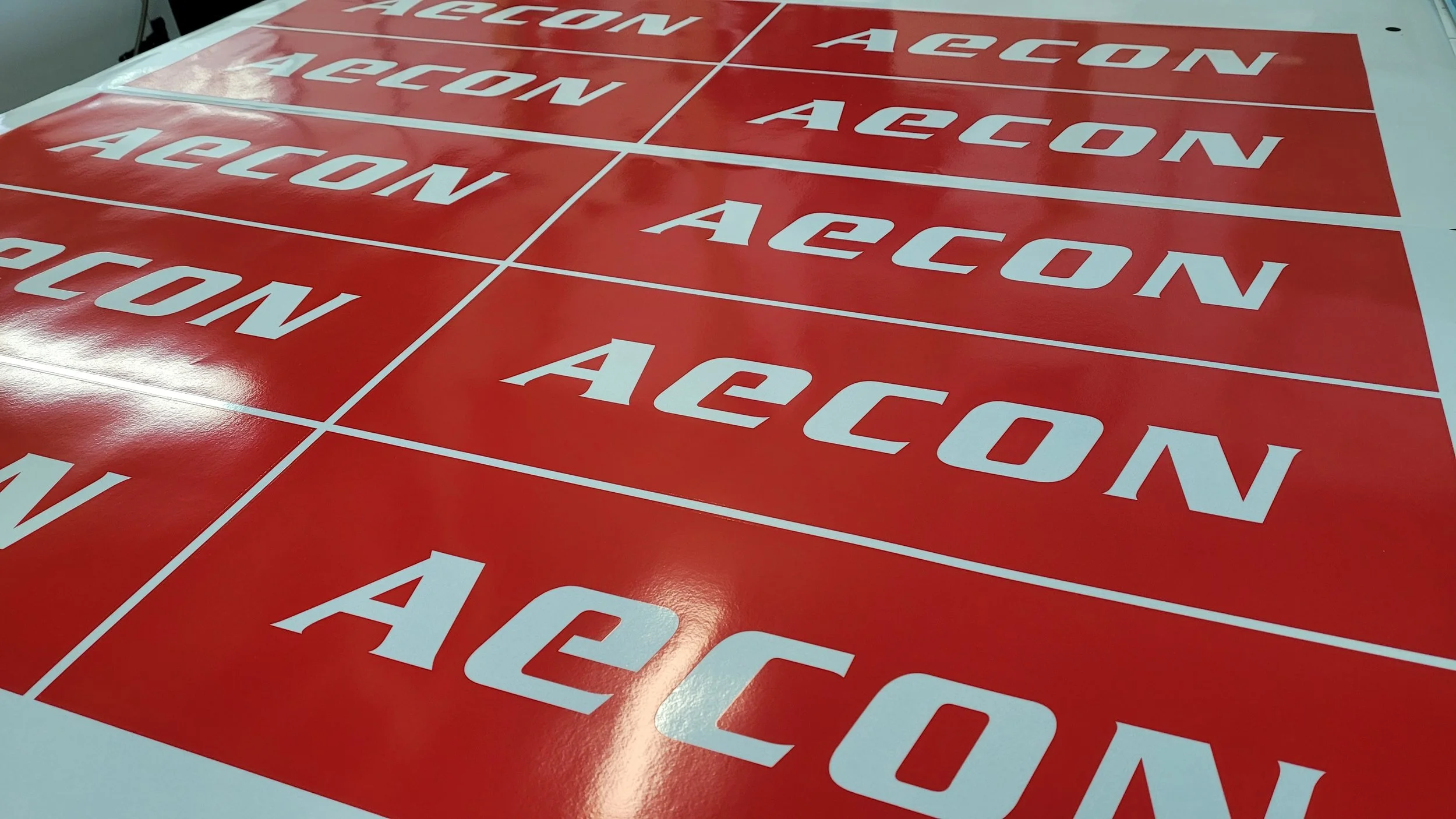 Multiple red sheets with the word 'AECON' printed in white, arranged in a grid pattern on a flat surface.