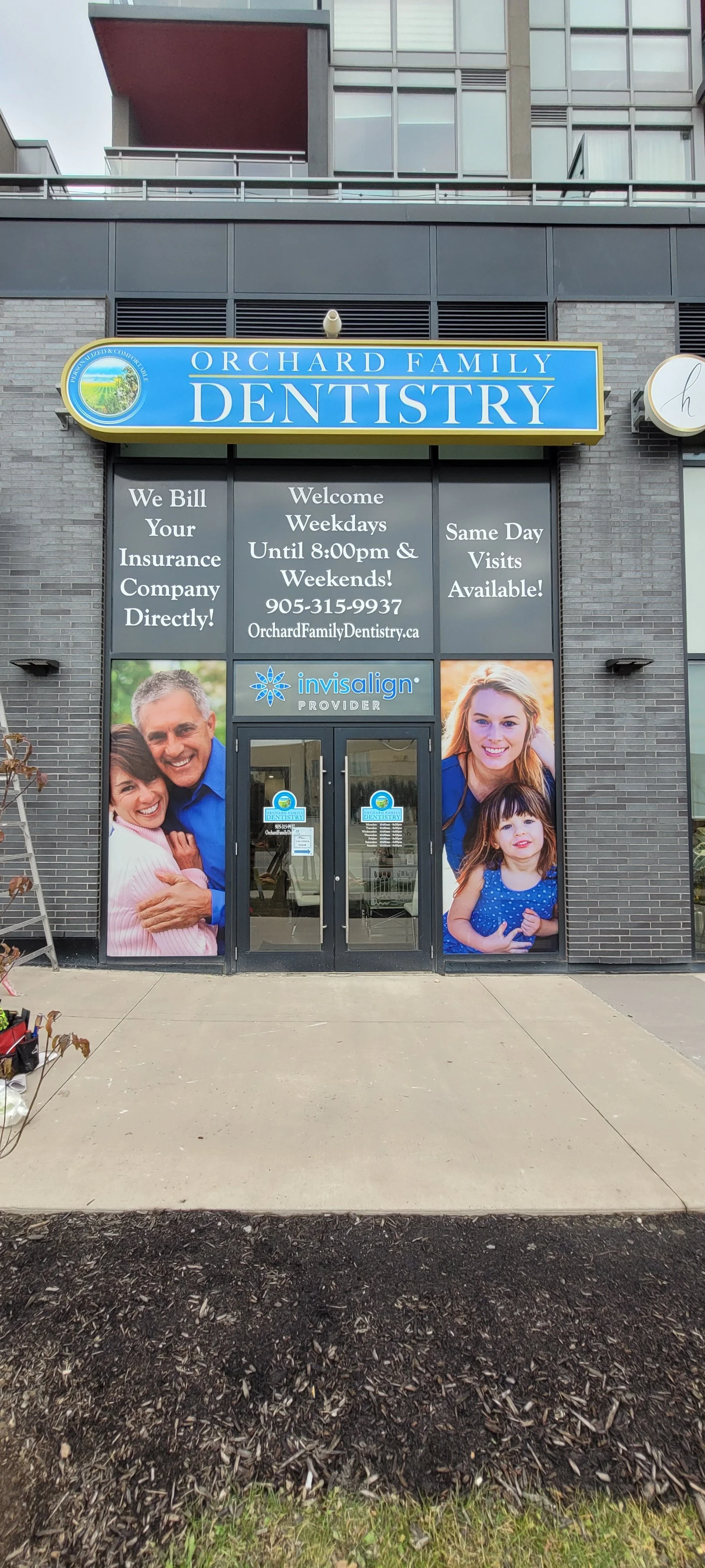 Exterior of Orchard Family Dentistry office with promotional posters, including a family photo, and signage indicating dental services and hours.