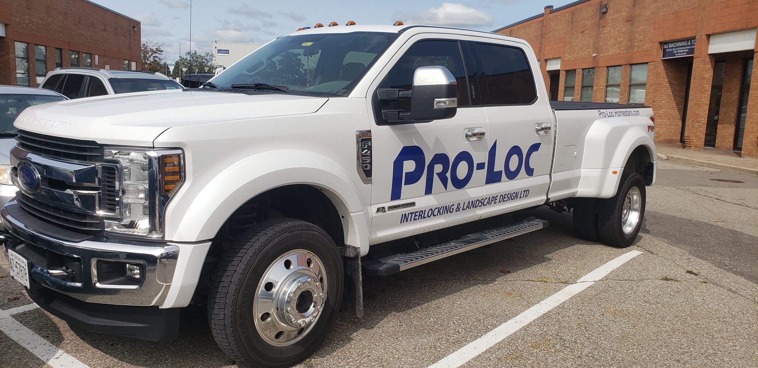White pickup truck with PRO-LOC branding parked in a parking lot with brick buildings in the background.