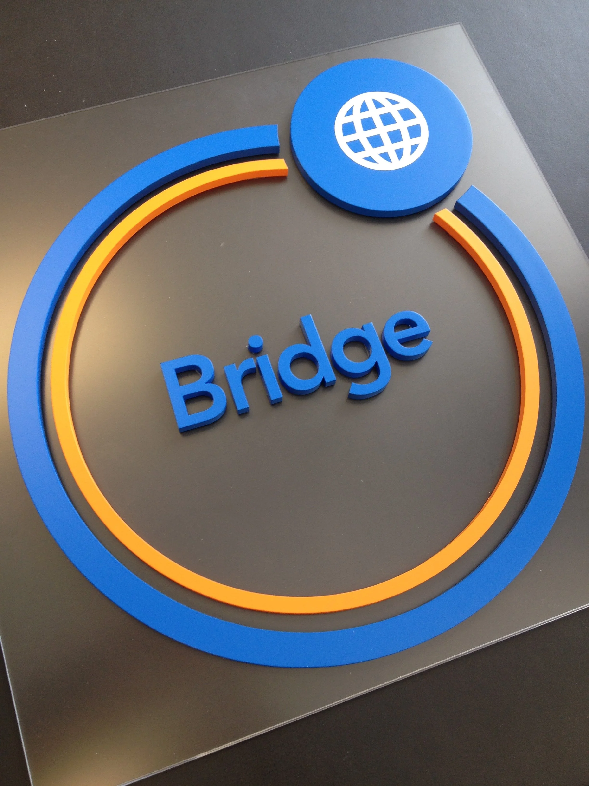 3D sign with the word 'Bridge' and a globe icon above it, surrounded by a partial circular blue and orange line.