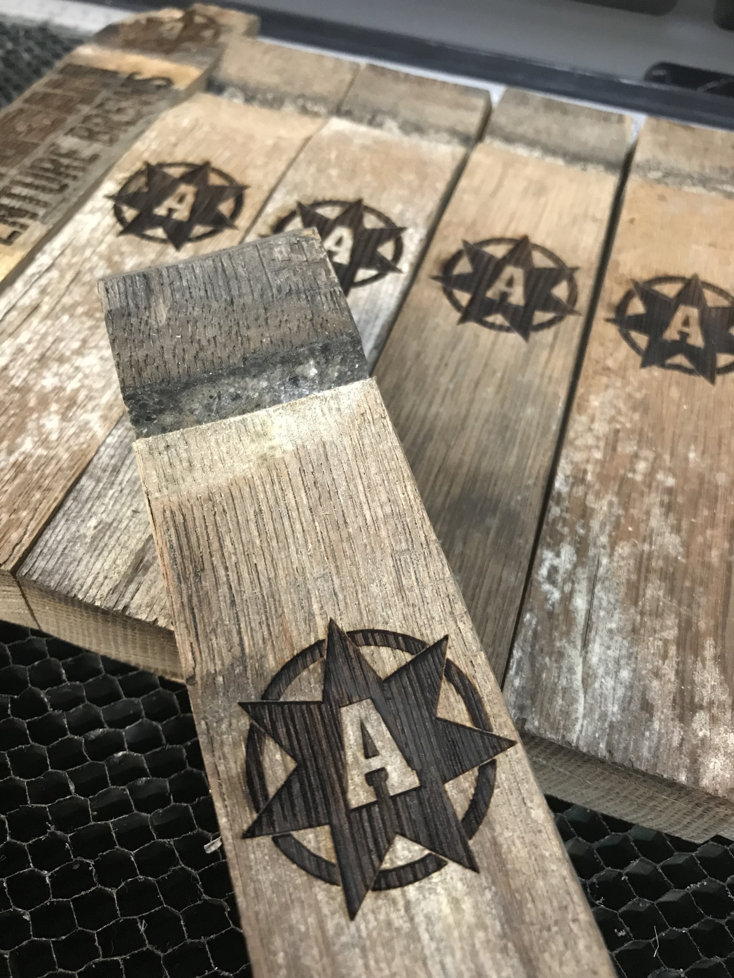 Multiple wooden planks with a star and letter 'A' burned into the surface, arranged on a metal grid.
