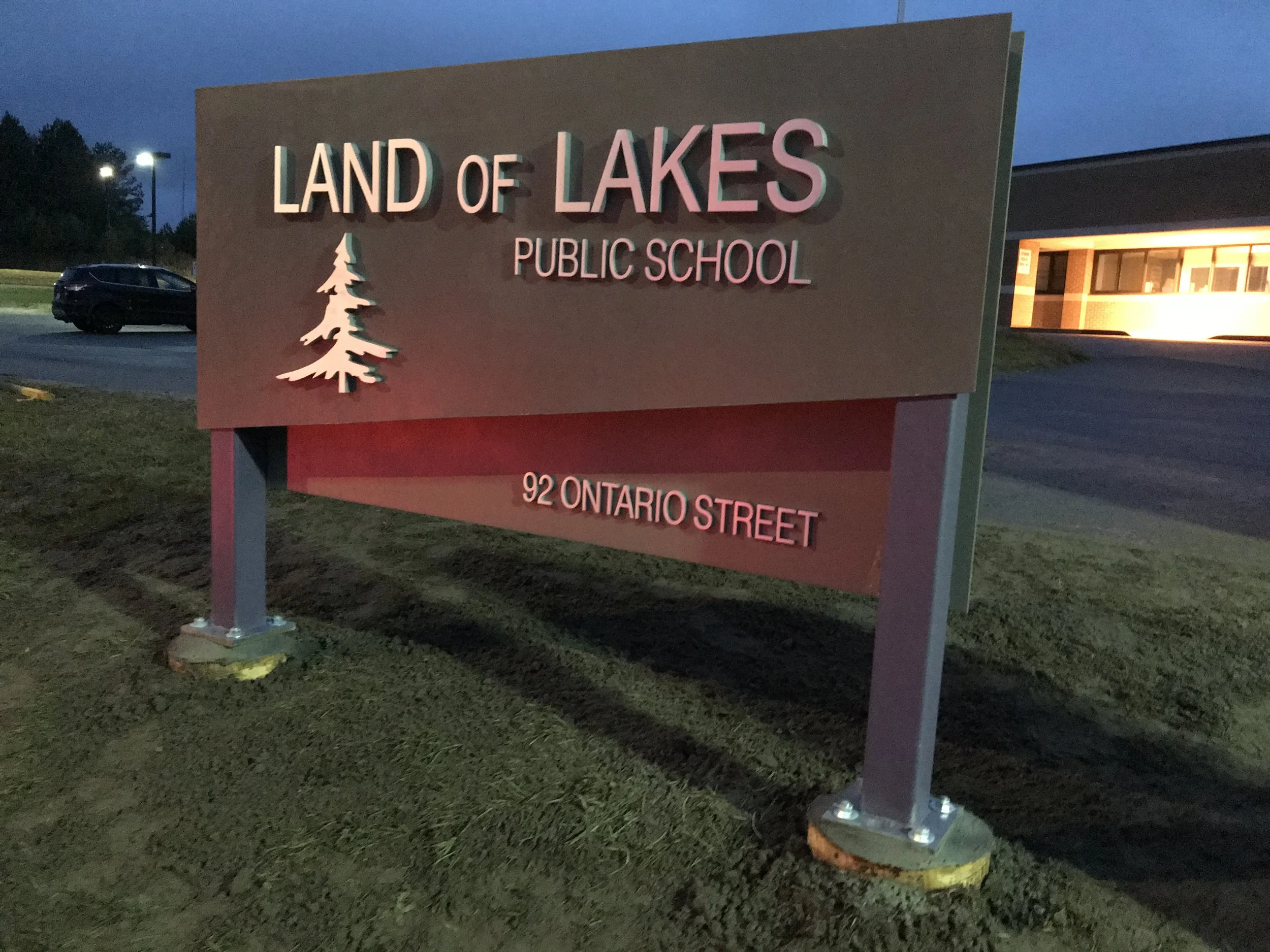 School sign for Land of Lakes Public School at 92 Ontario Street, illuminated during dusk. The sign features a tree graphic.
