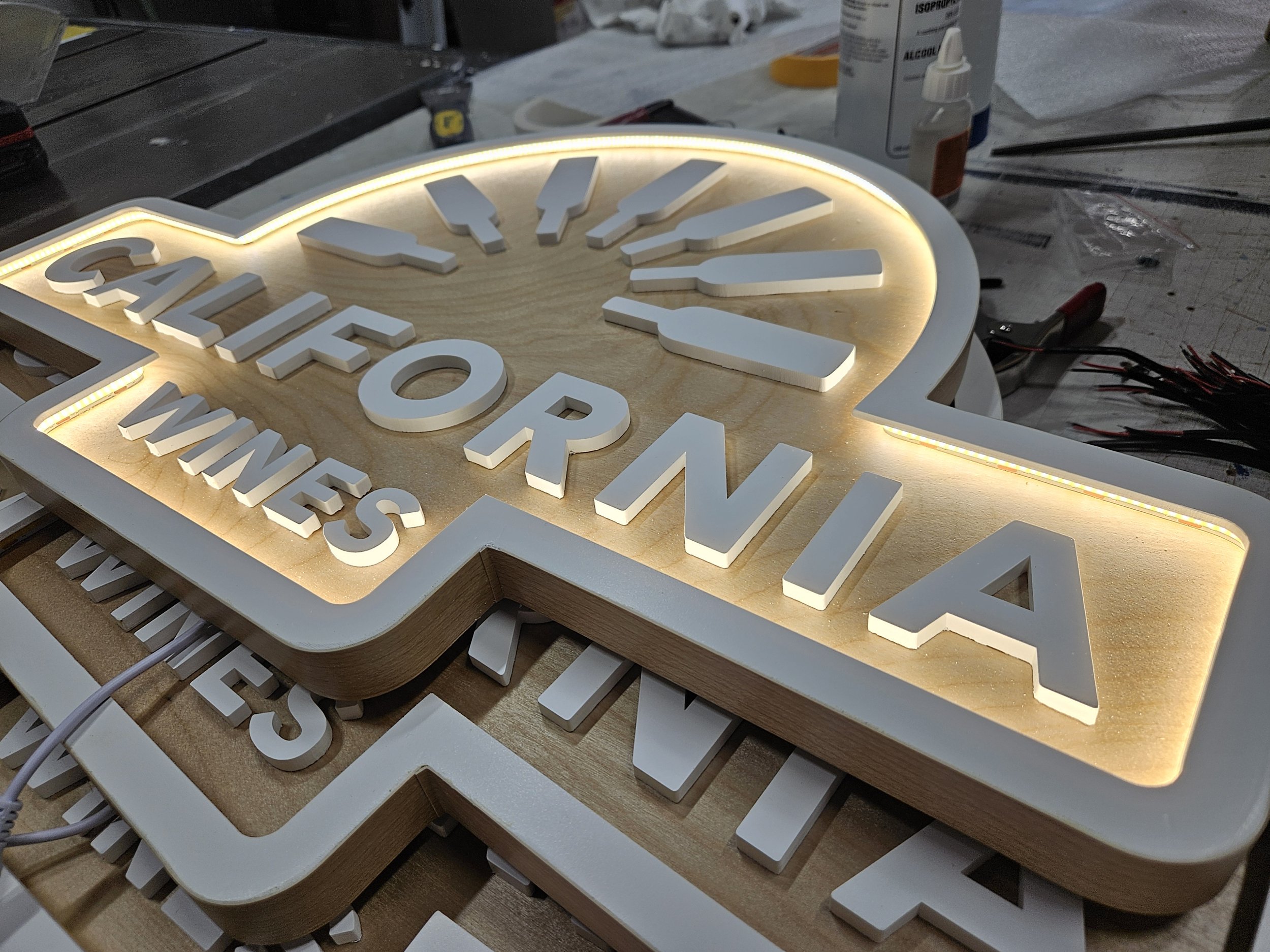 A wooden and illuminated sign with the words 'California Wines' lying on a worktable with tools and supplies around.