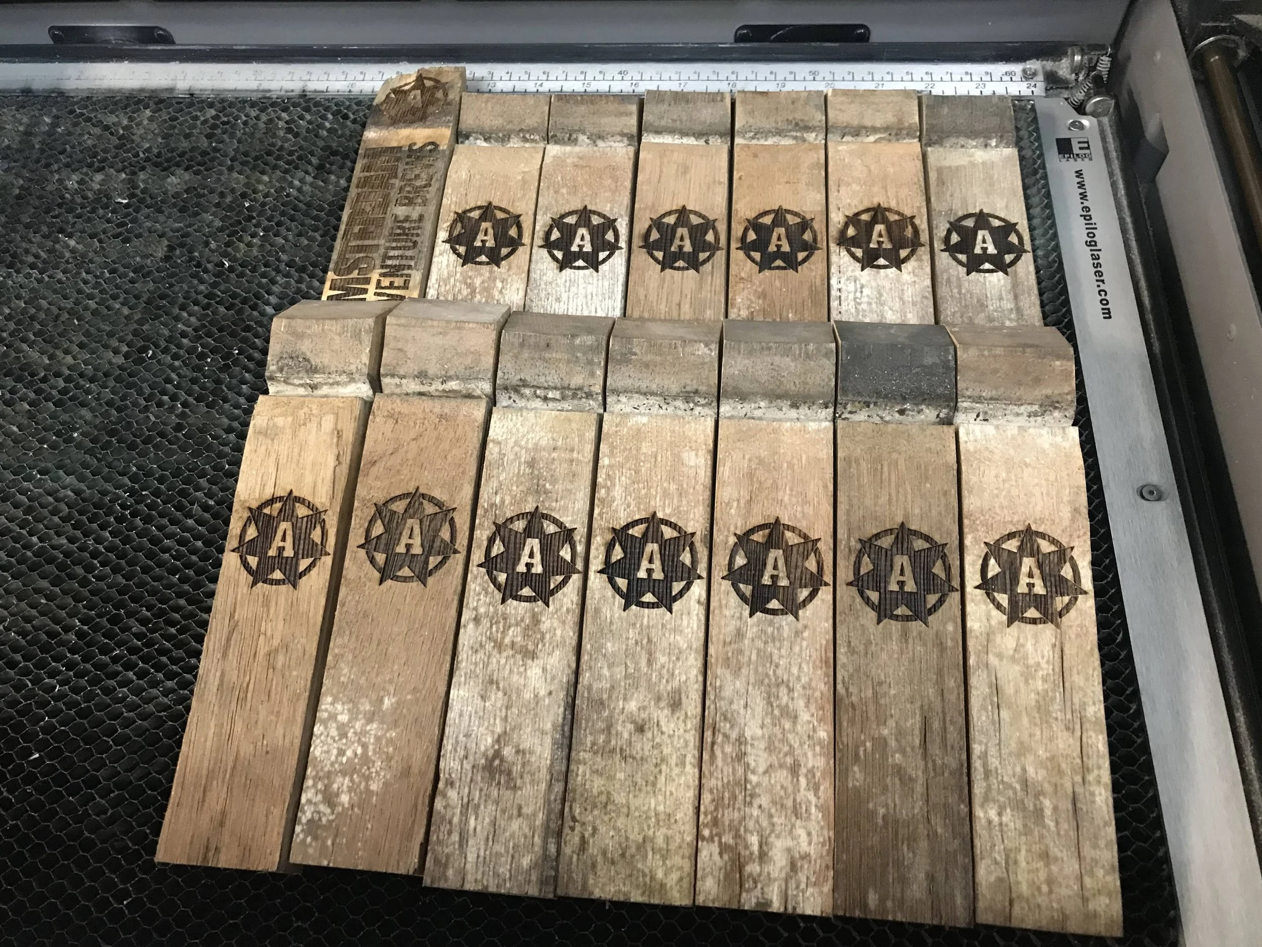 A laser cutter engraved wooden pieces with a star and the letter 'A' in the center, arranged on a cutting surface.