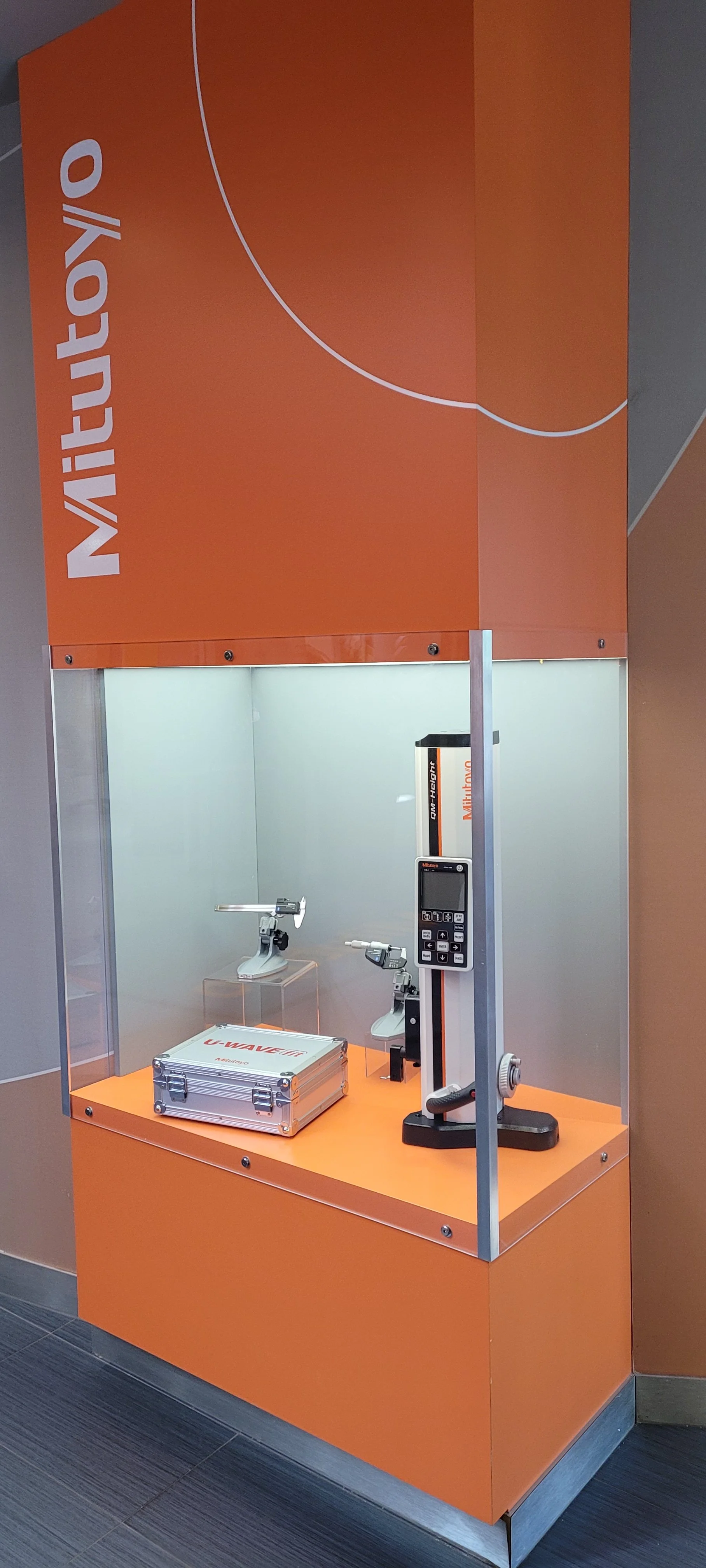 Display of a product in a glass enclosure, branded with the Mitutoyo logo and orange color.