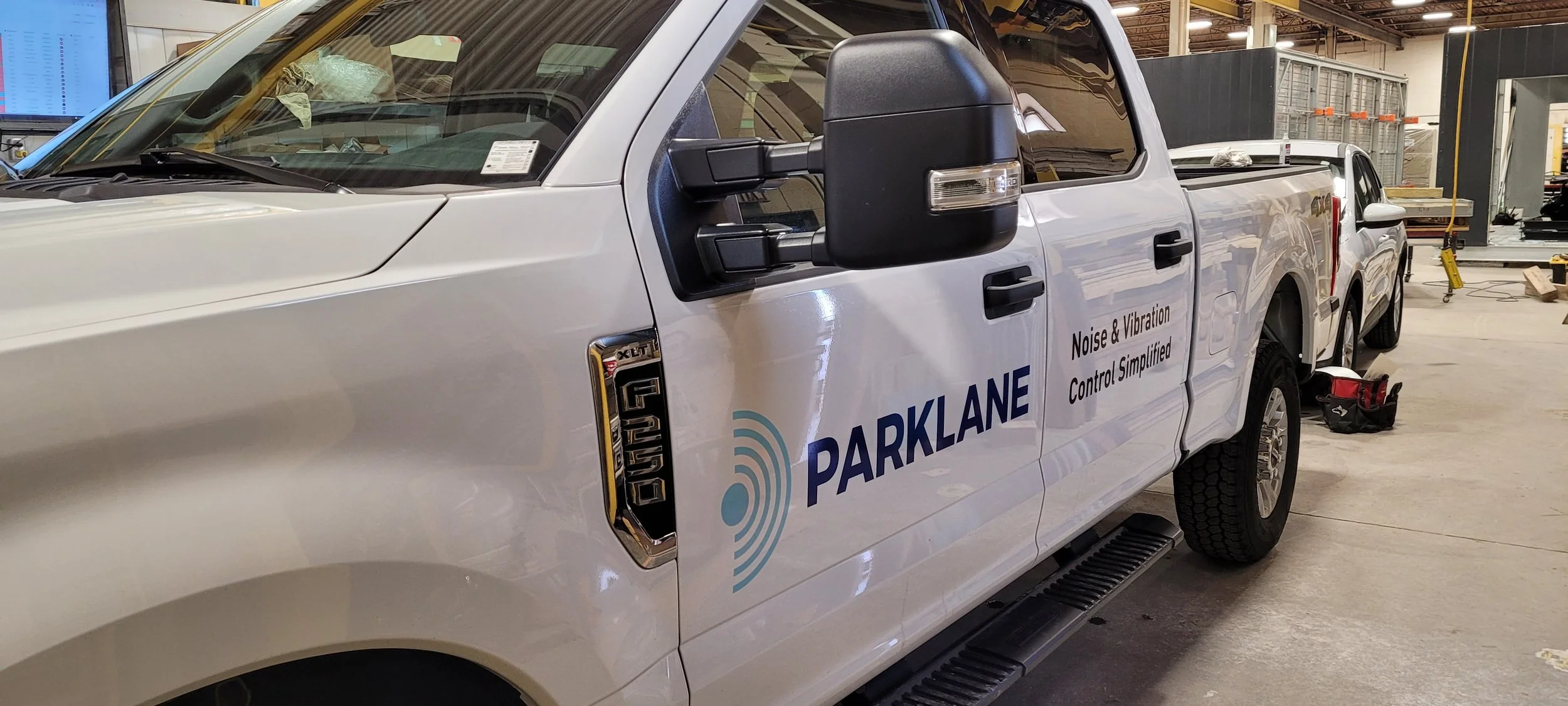 White Ford F-150 truck with Parklane logo and sign that reads 'Noise & Vibration Control Simplified' parked inside a warehouse or garage.