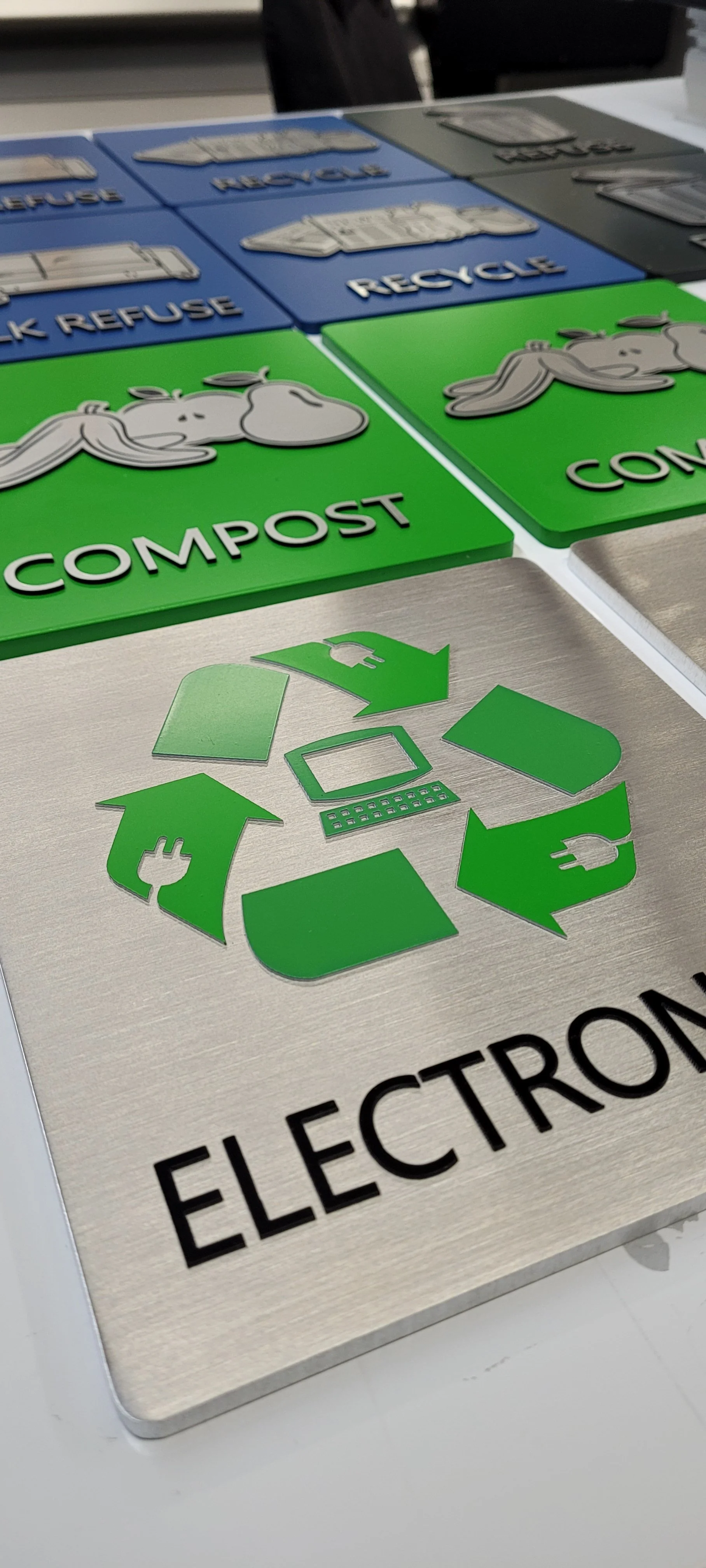 Colorful signage with recycling, compost, and electronic waste symbols on a table.