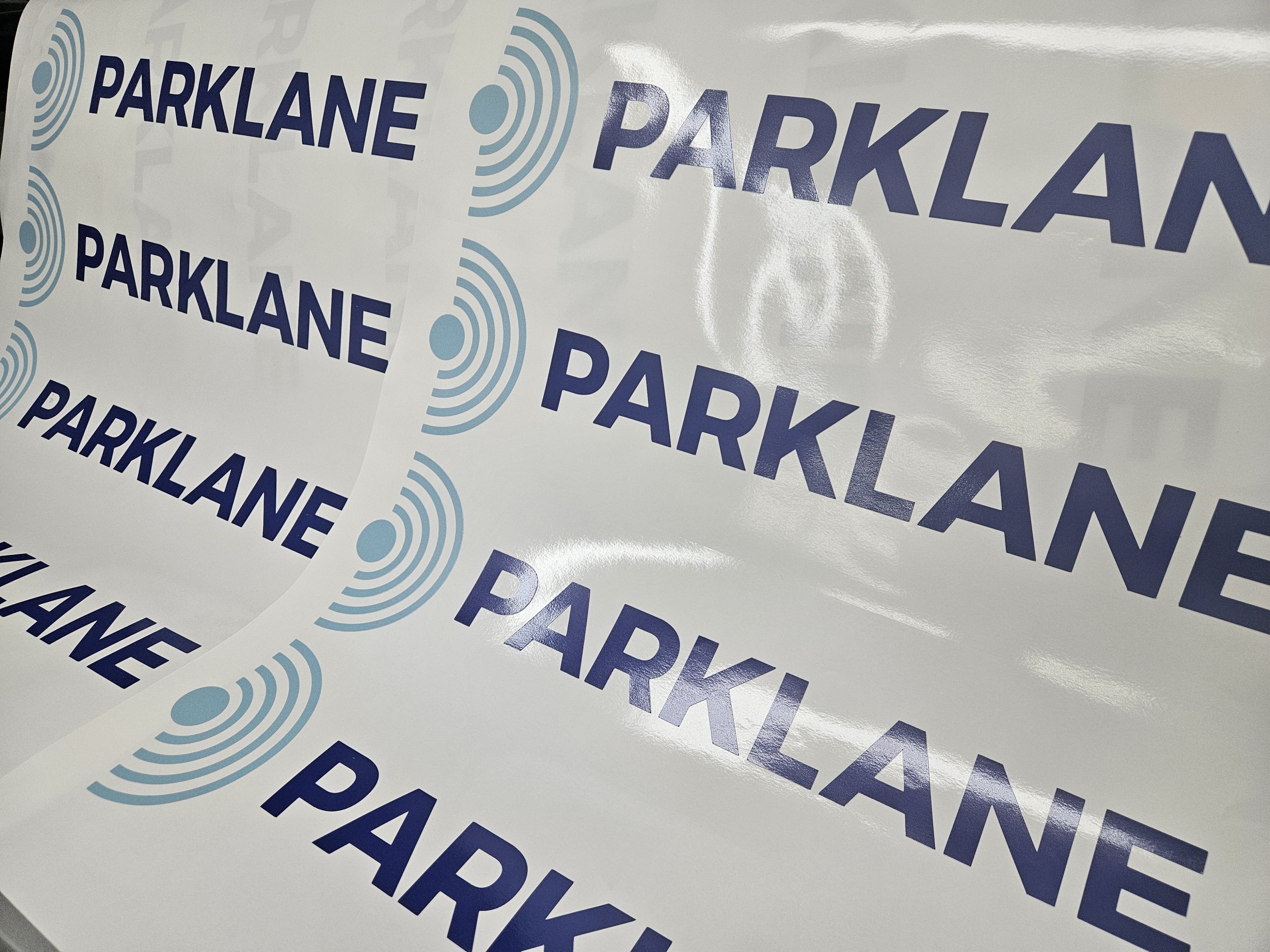 Sheet of stickers with the word 'PARKLANE' in dark blue uppercase letters next to a blue concentric circle symbol, repeated multiple times.