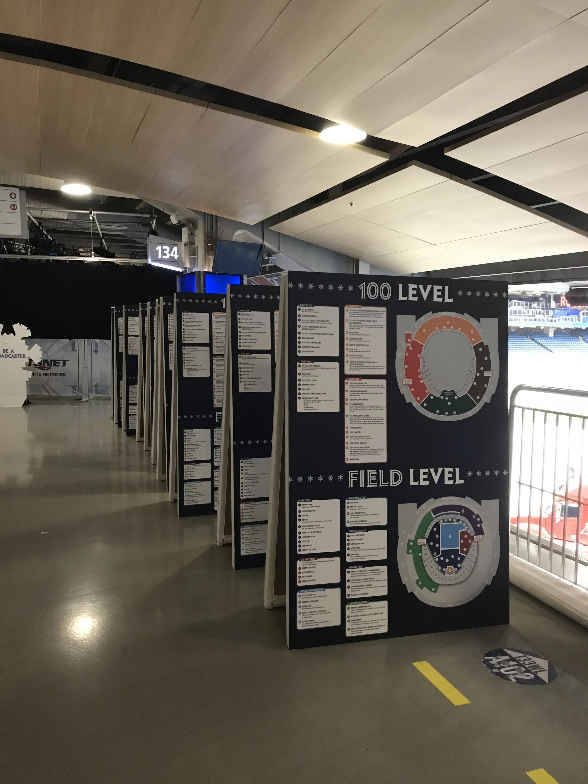Information boards in a stadium with seating and field in the background, displaying maps for 100 level and field level sections.