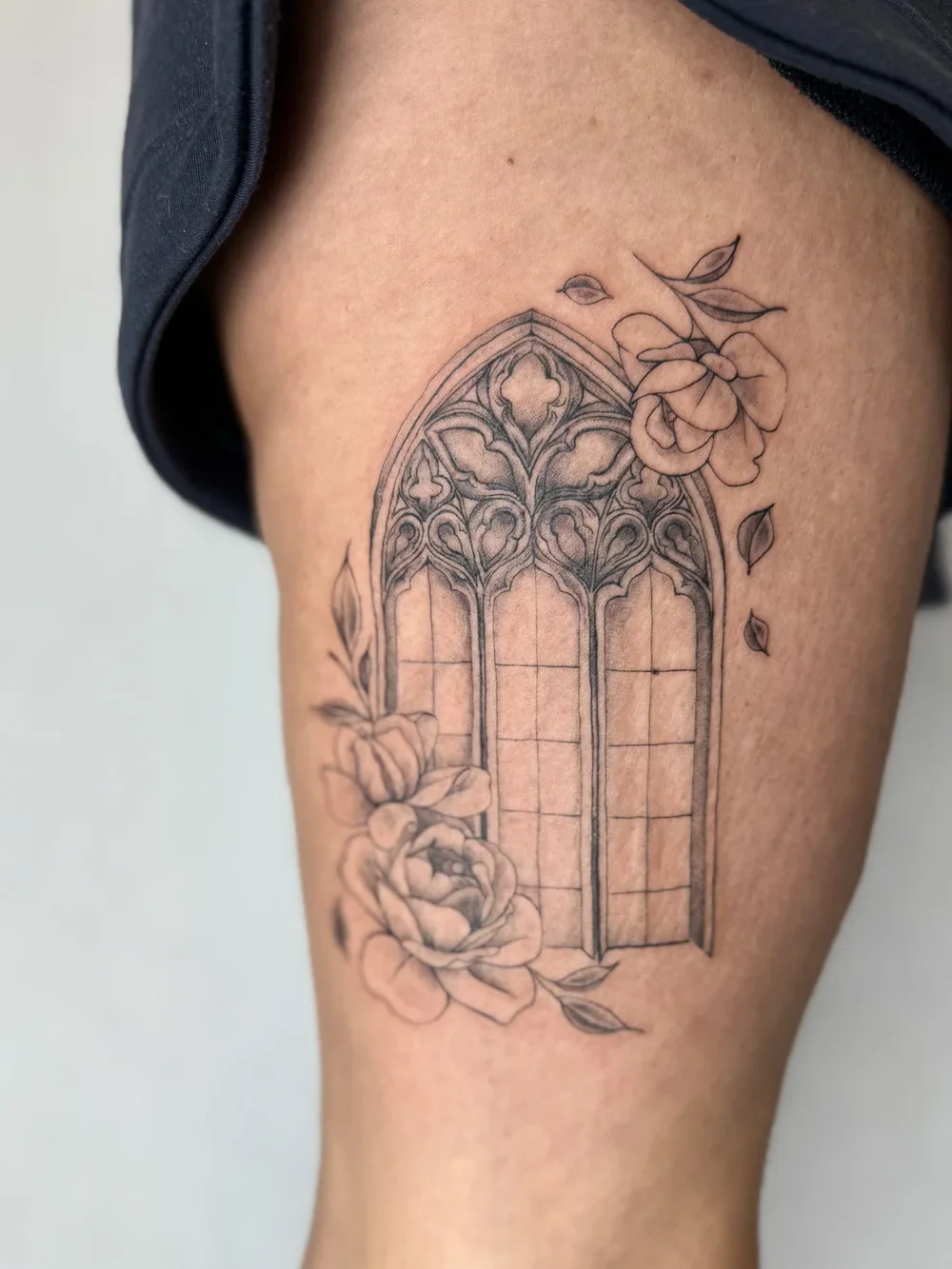 Tattoo of a decorative arched window with floral designs and roses on the person's thigh.