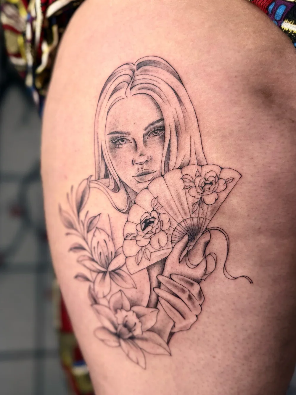 Line art tattoo of a woman holding a fan with flowers, detailed face with freckles and long hair.