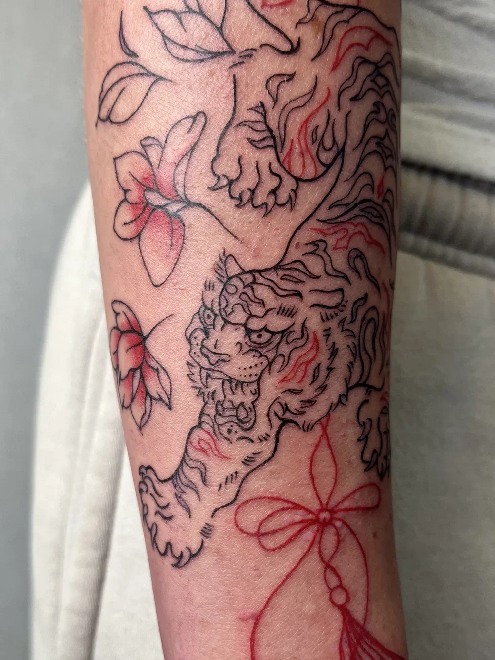 Tattoo of a lion's face with leaves and a bow on the arm.