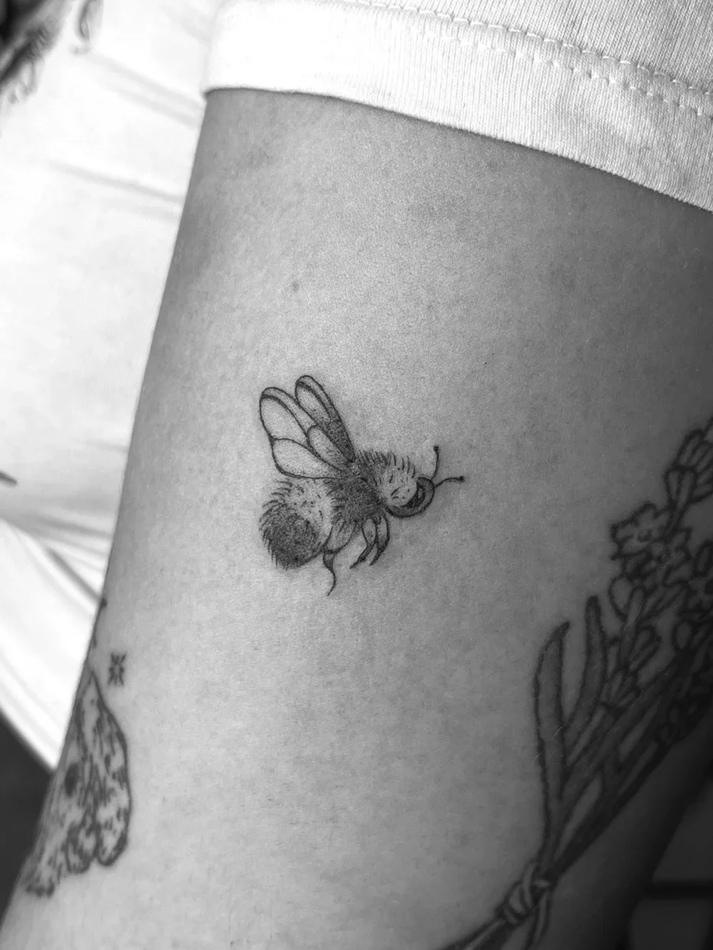 Tattoo of a bee on a person's upper arm, with other tattoos visible nearby.