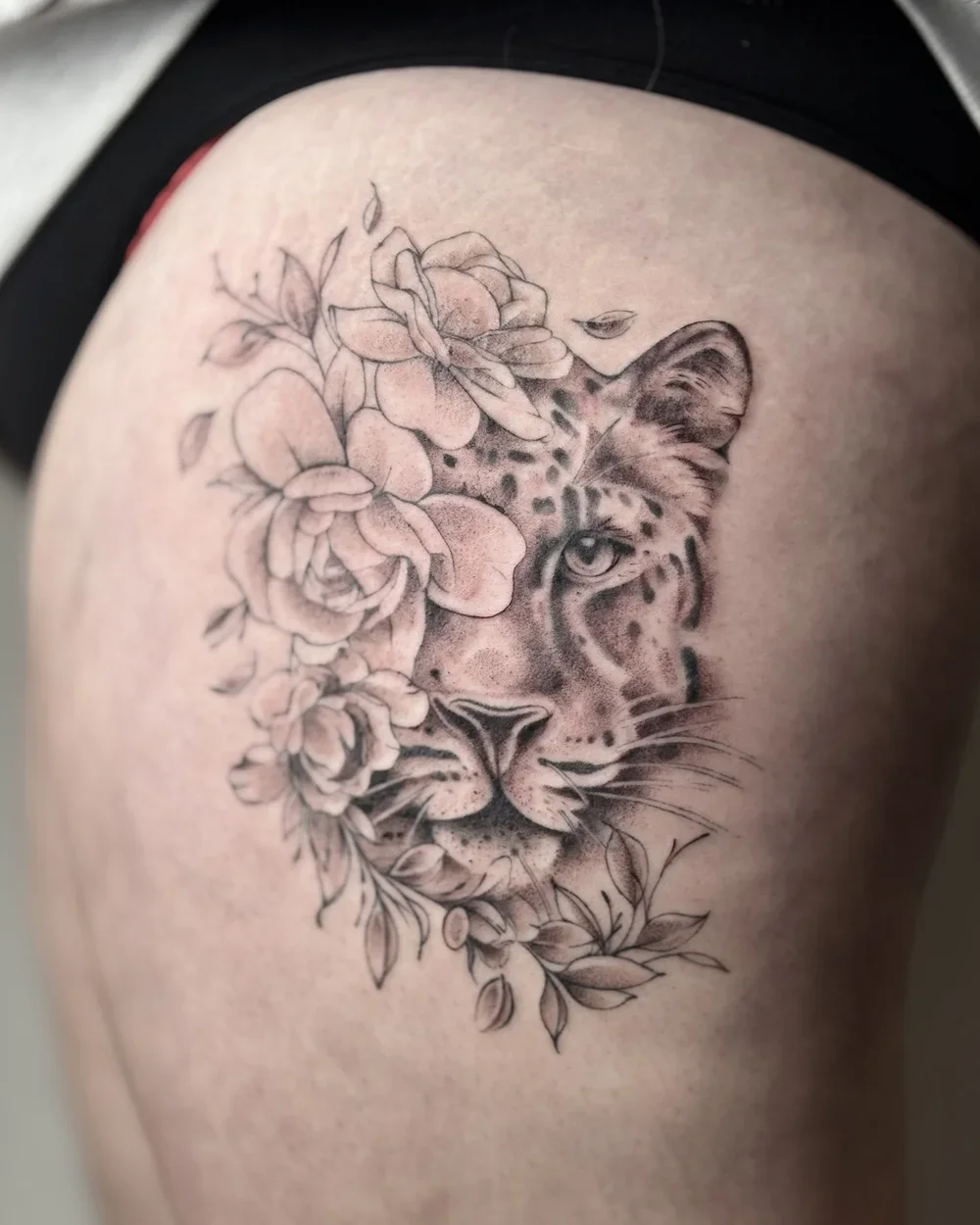 Tattoo of a leopard's face partially covered with flowers on a person's skin.