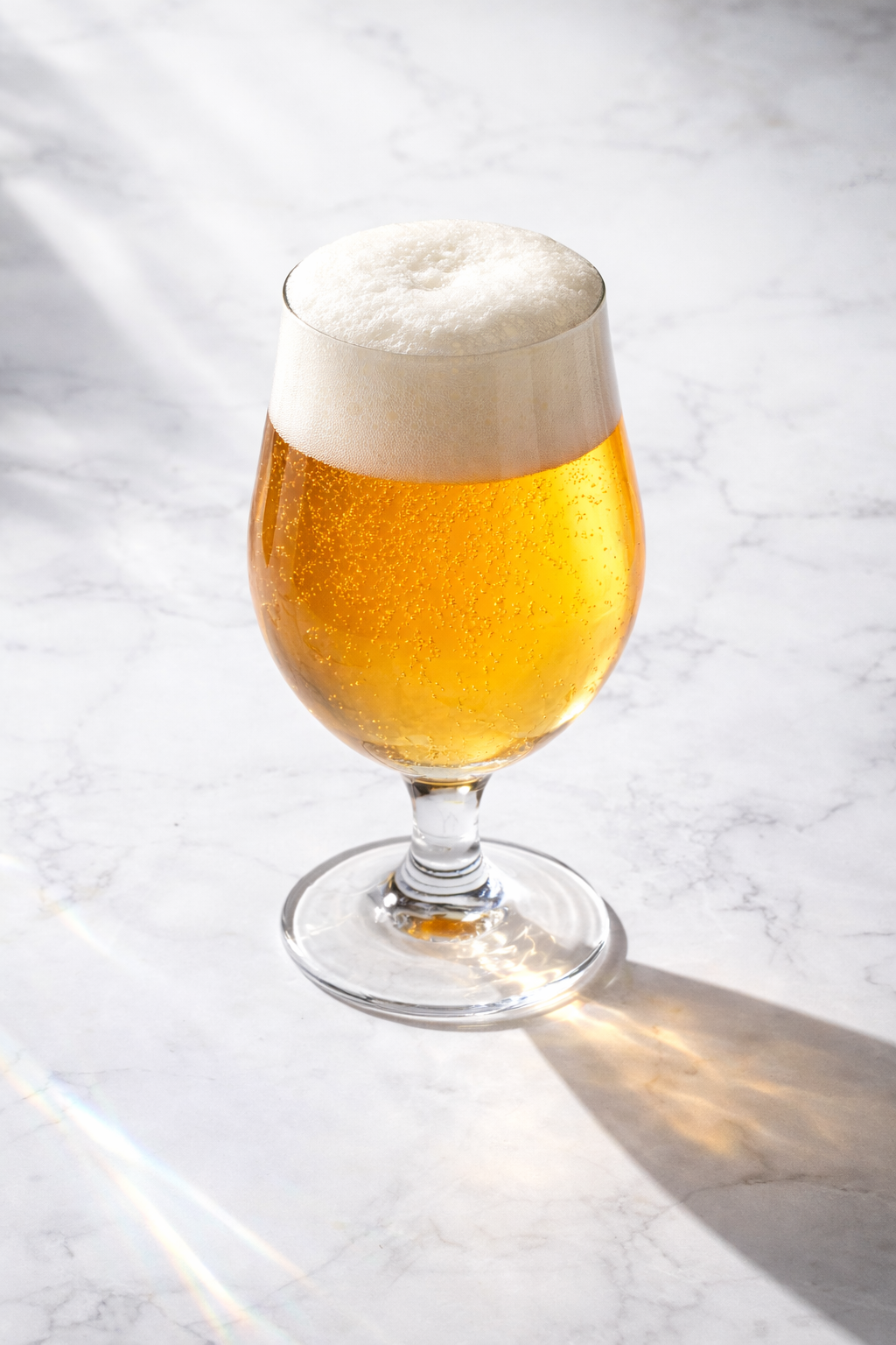 Ein Glas Bier mit Schaum auf einem weißen Marmortisch, Sonnenlicht wirft einen Schatten.