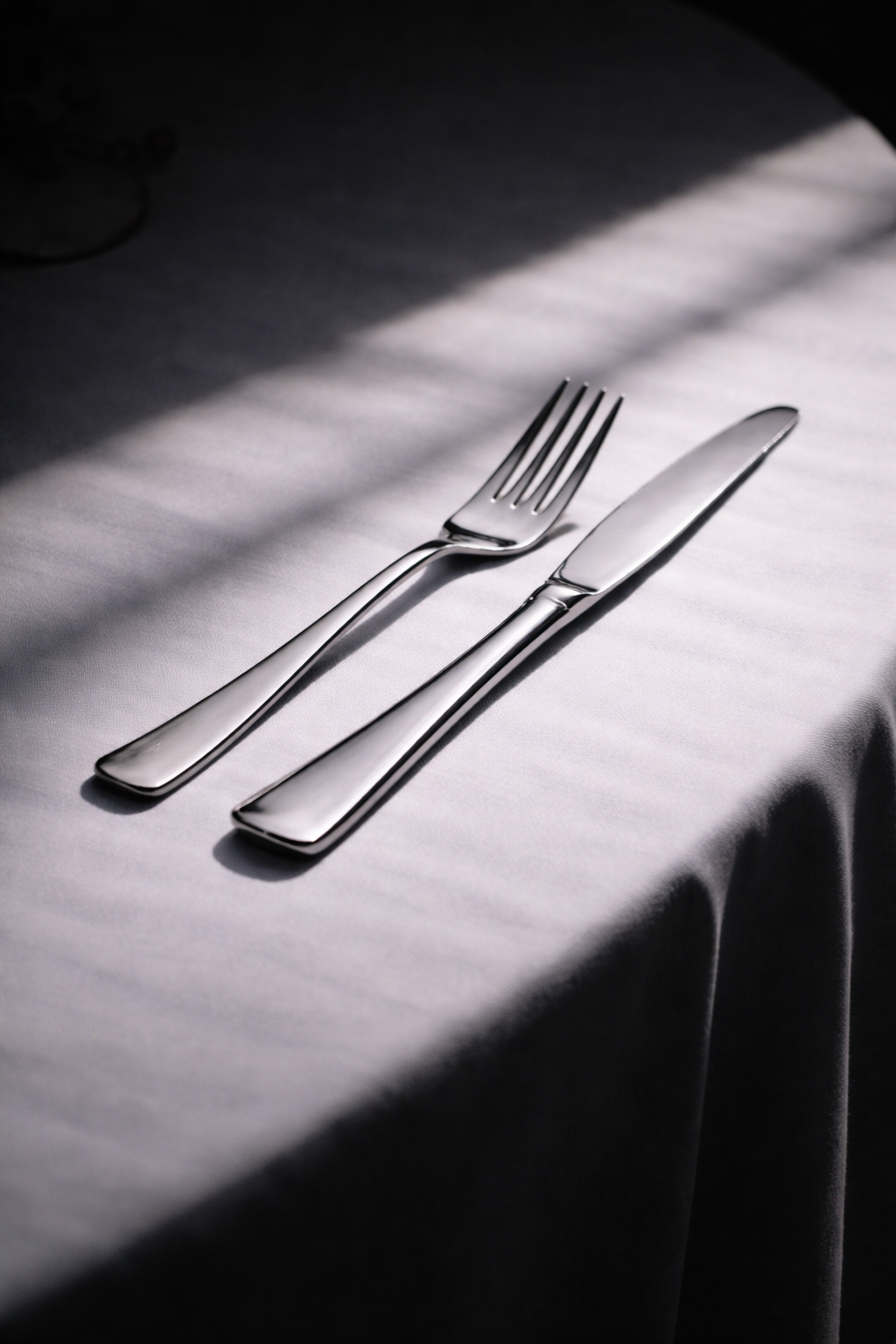 ein Besteckset mit Messer und Gabel auf einem weißen Tischlaken, mit Licht- und Schatteneffekten.