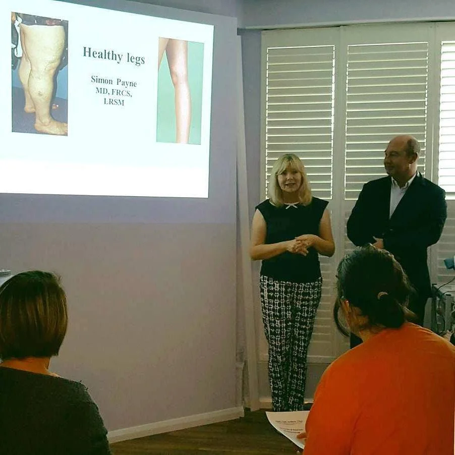 A woman and a man standing in front of a presentation slide about healthy legs, with an audience seated in front.