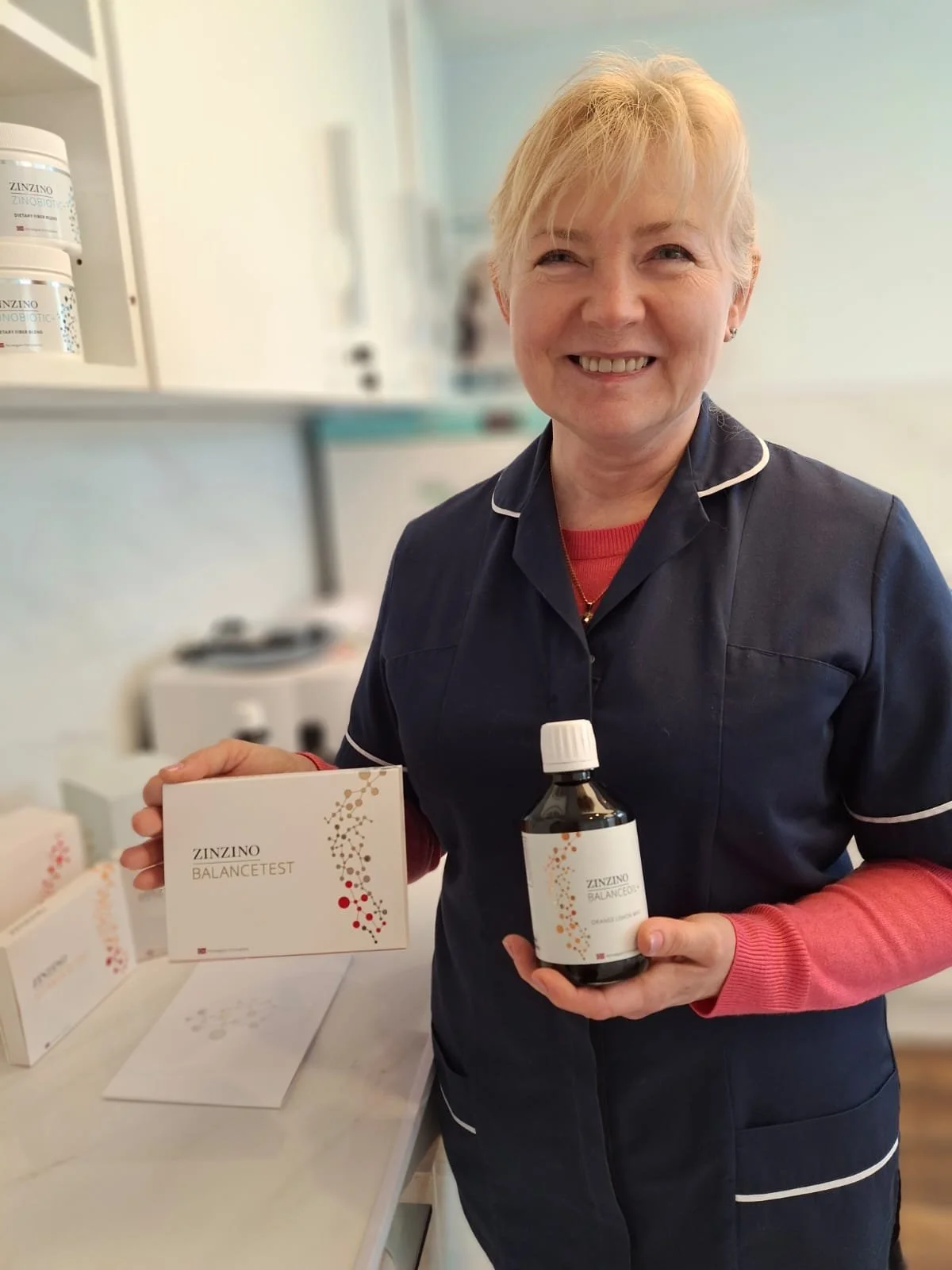 Smiling healthcare worker holding Zinzino BalanceTest box and bottle in a clinical setting.