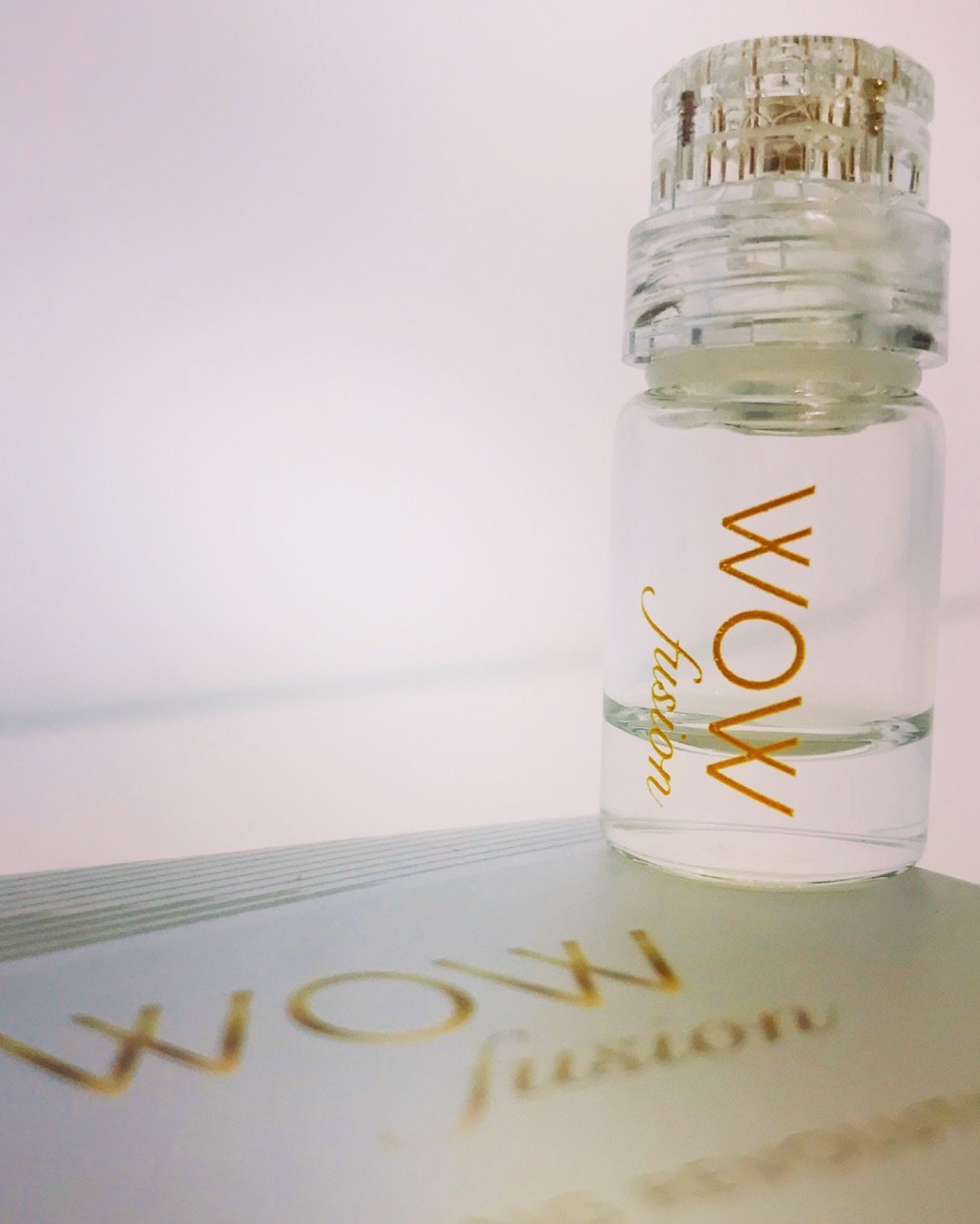 A small glass bottle labeled 'Vow' appears to be a perfume or essential oil bottle, placed on top of a white surface with a reflection.