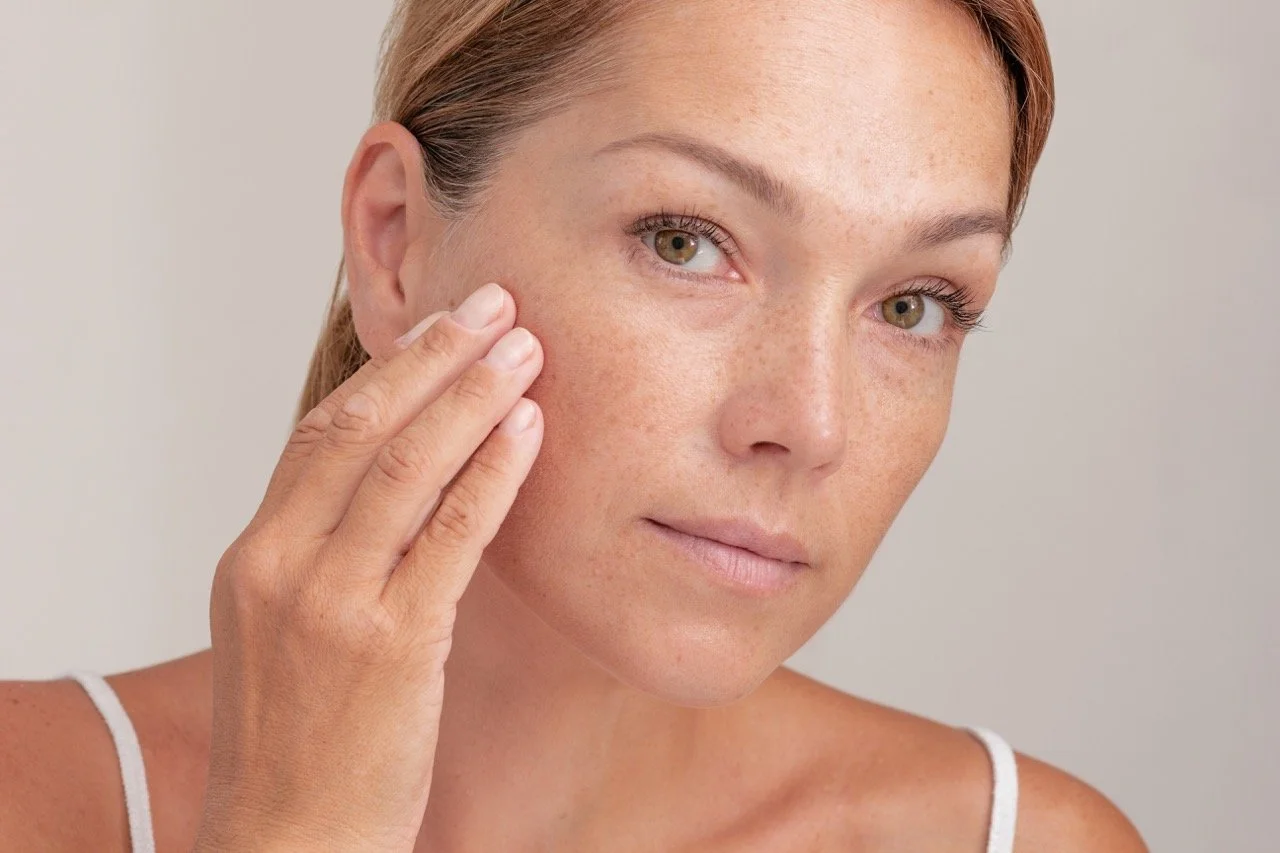 A woman with clear skin and freckles gently touching her face with her fingers.