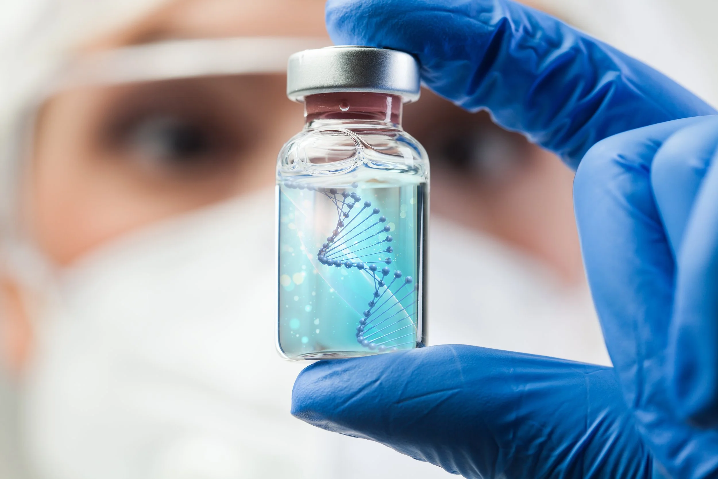 A scientist wearing a white mask and blue gloves holding a small vial filled with liquid that contains a digital illustration of a DNA double helix.
