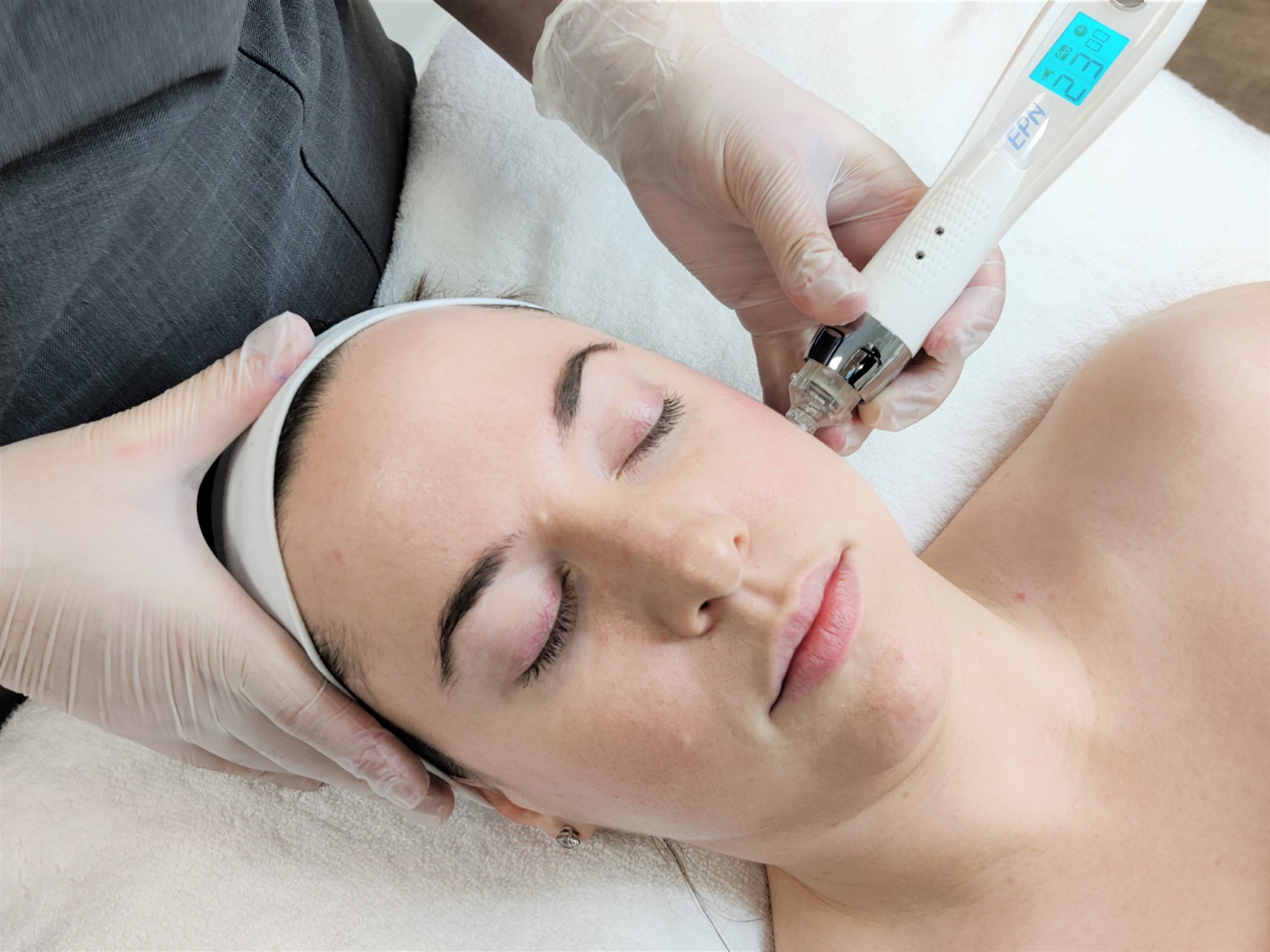 A woman receives a skincare treatment with a device on her face while lying down with eyes closed.