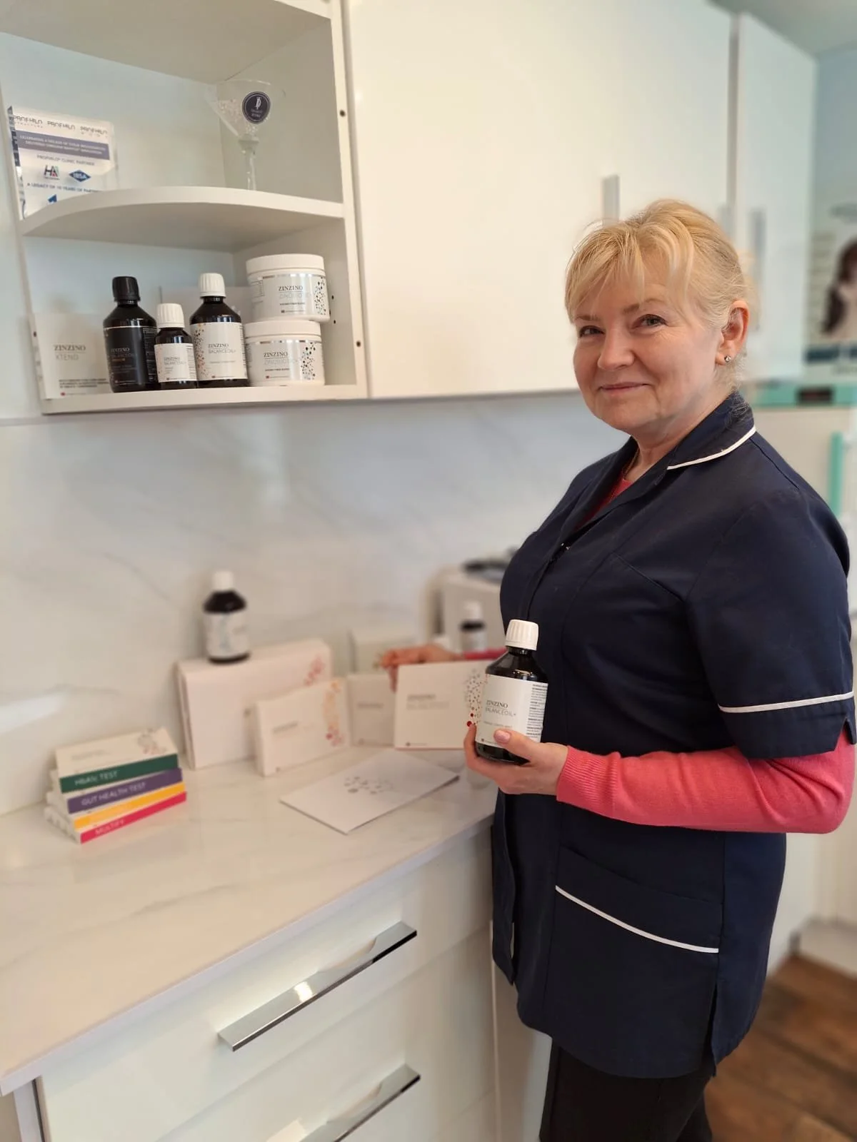 A healthcare worker holding a bottle of medication in a medical office with shelves of supplies and pamphlets.