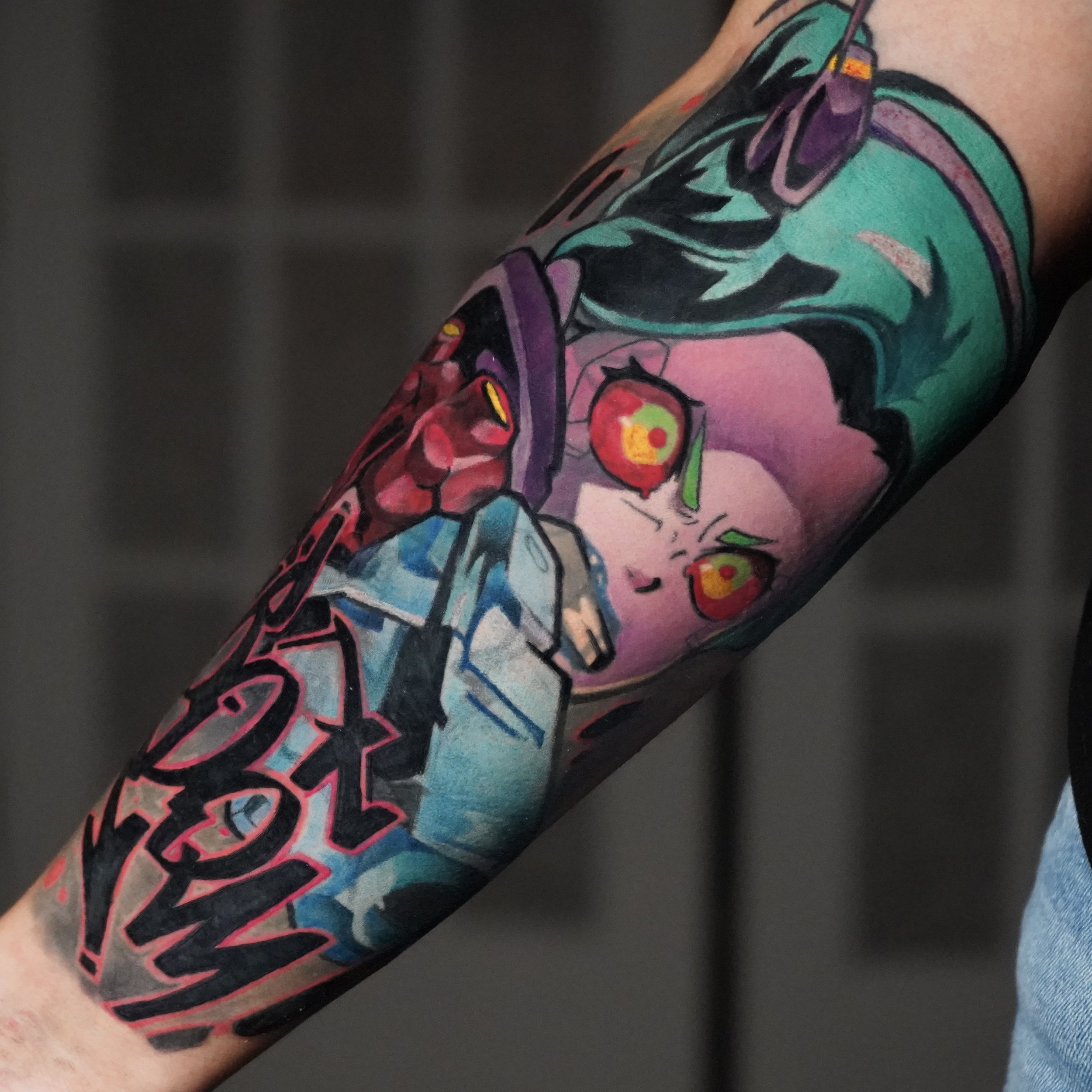 Colorful tattoo of a girl with pink hair and green eyebrows, holding a spray paint can, with red eyes and graffiti-style lettering on the arm.