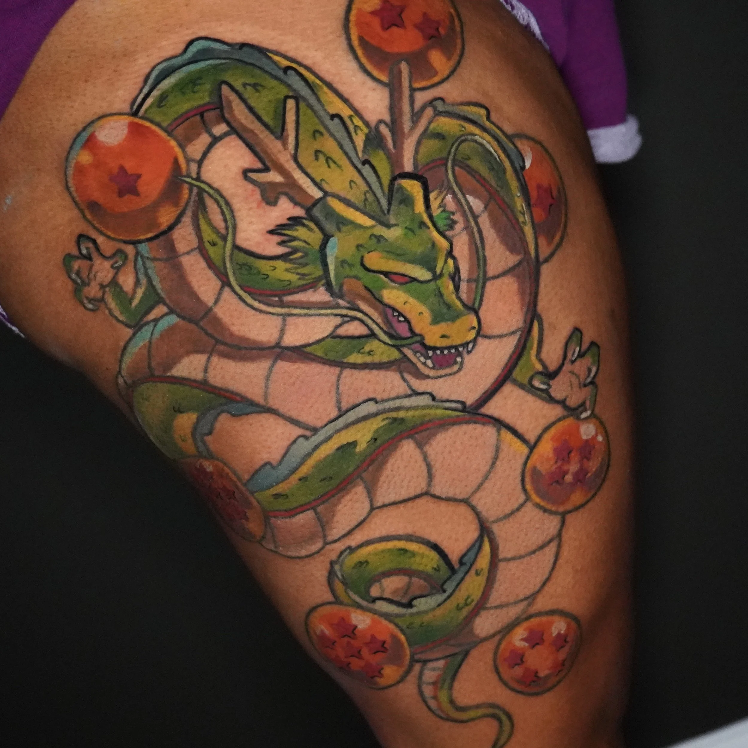 A colorful tattoo of a dragon intertwined with seven orange dragon balls with red stars on a person's thigh.