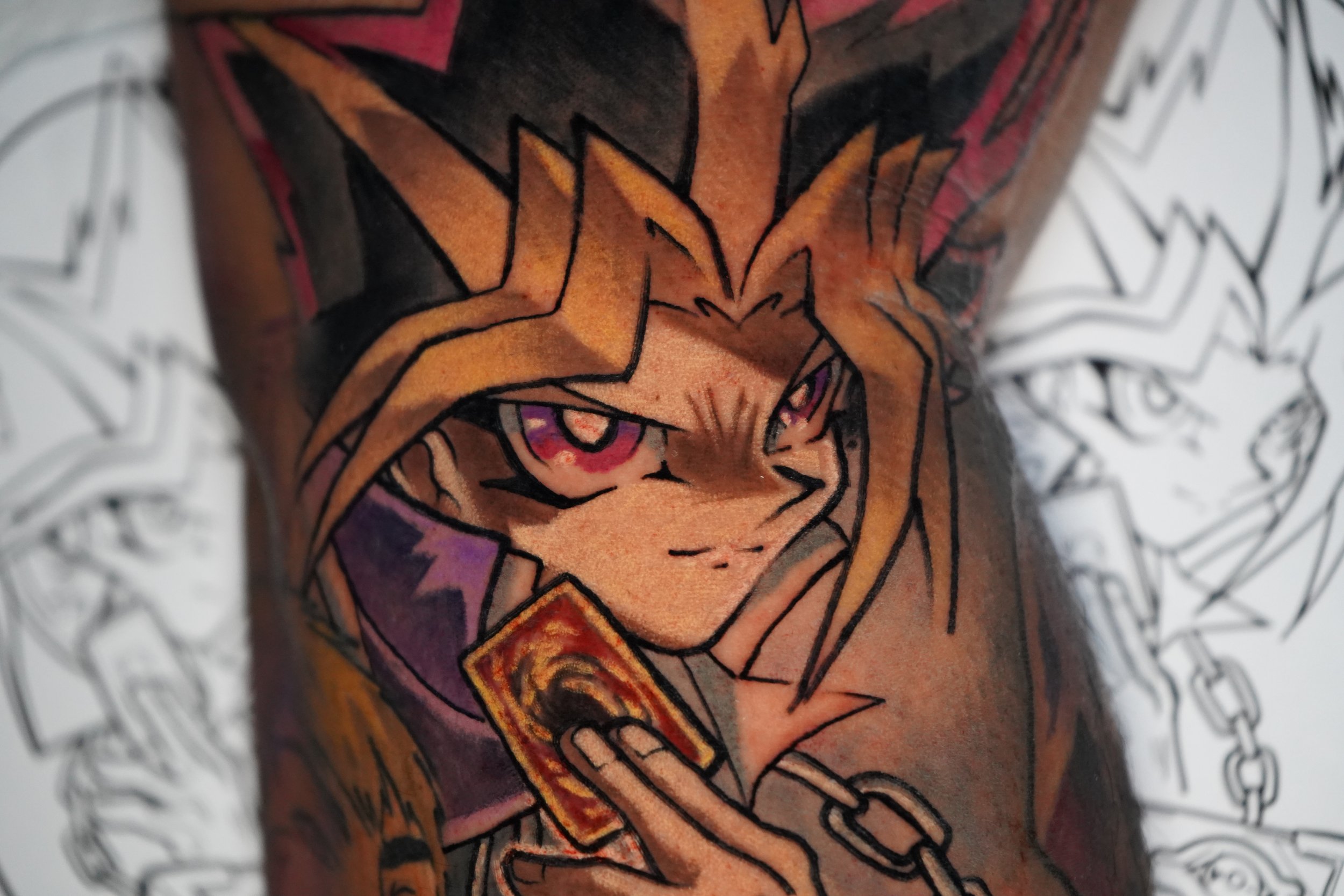 Tattoo of a cartoon character with blond hair, purple eyes, and a smirking expression, holding a card, with a chain around their neck, on a person's arm.