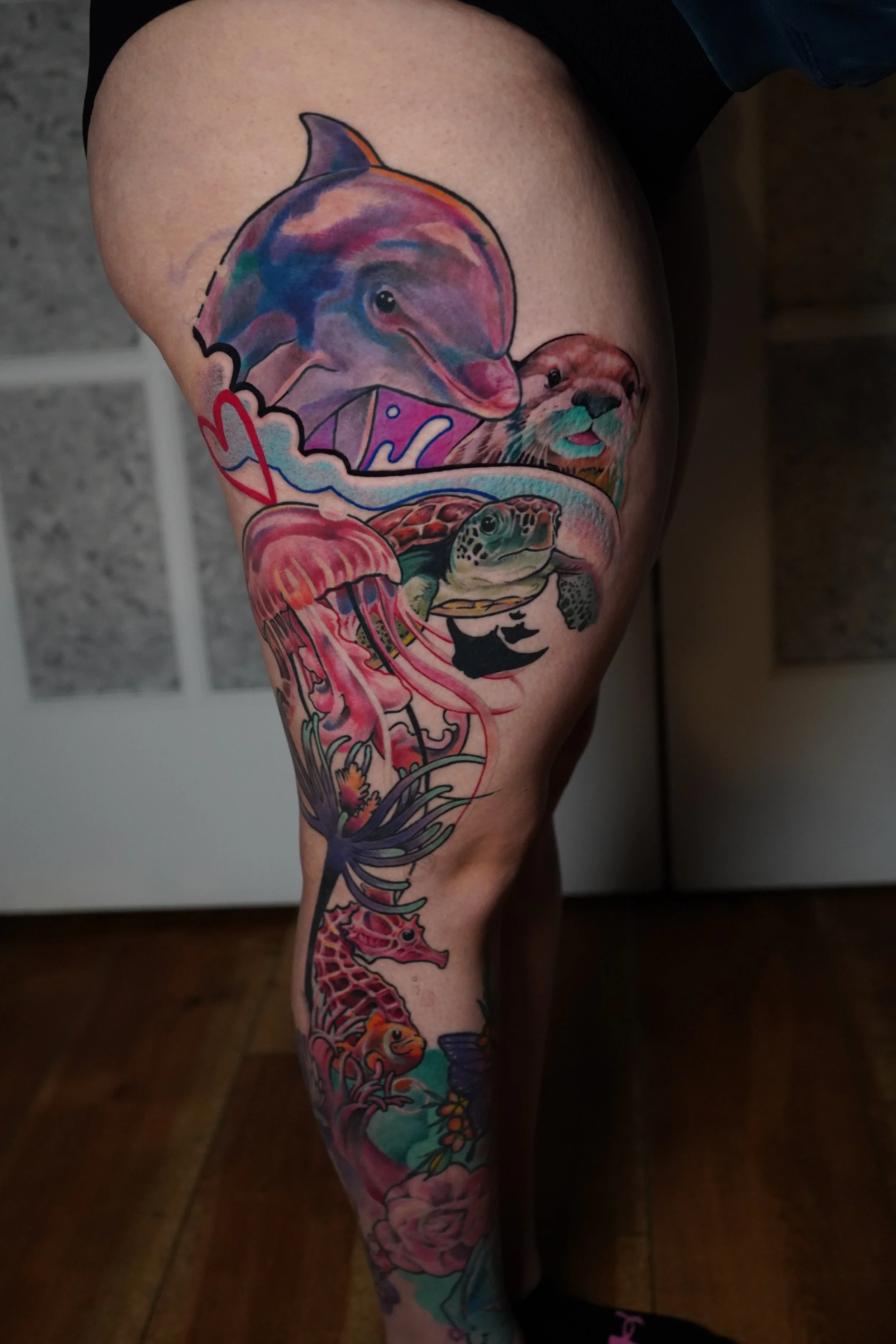 Colorful tattoo on a person's thigh featuring marine animals such as a dolphin, turtle, jellyfish, octopus, and a giraffe.