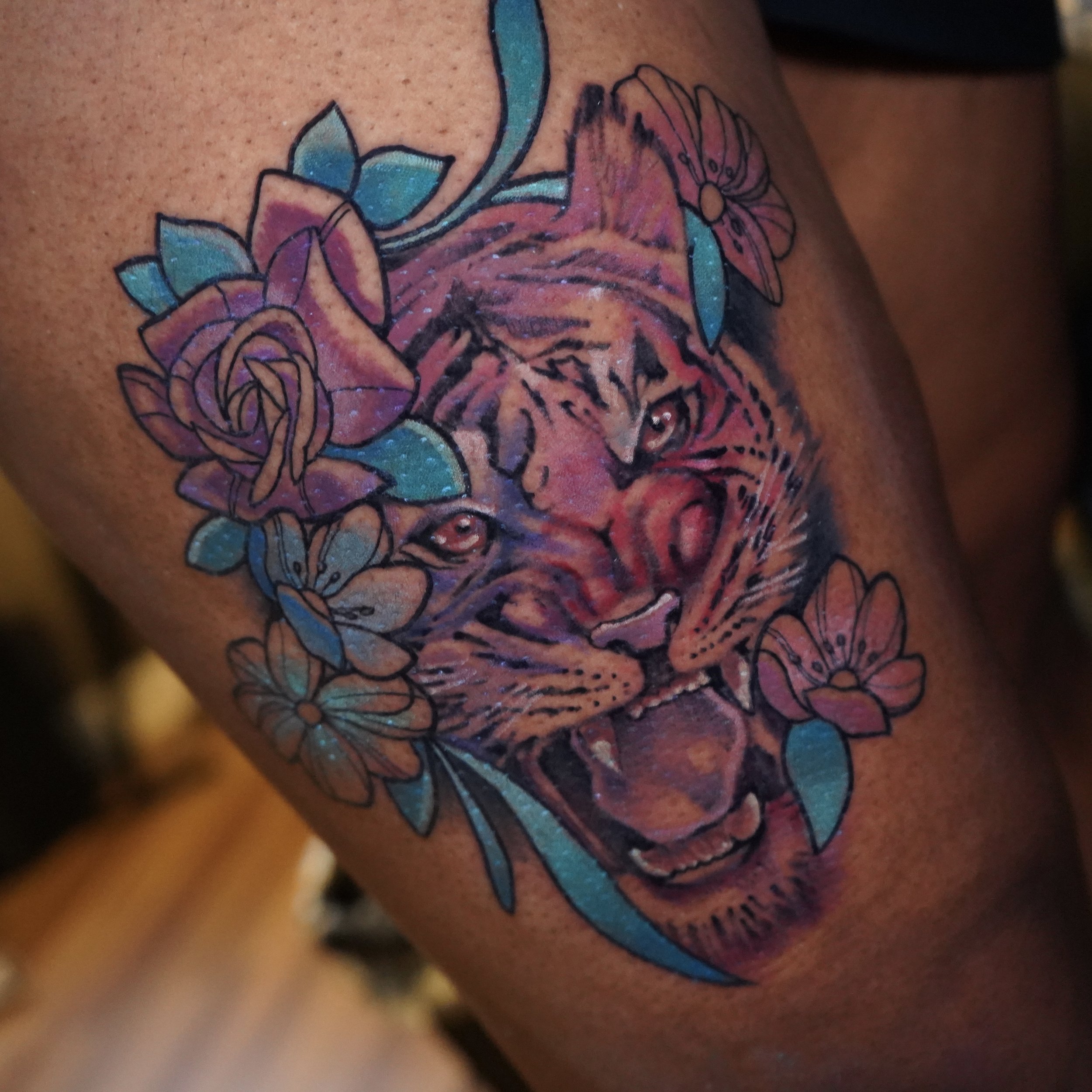 Tattoo of a tiger's face surrounded by pink and blue flowers.