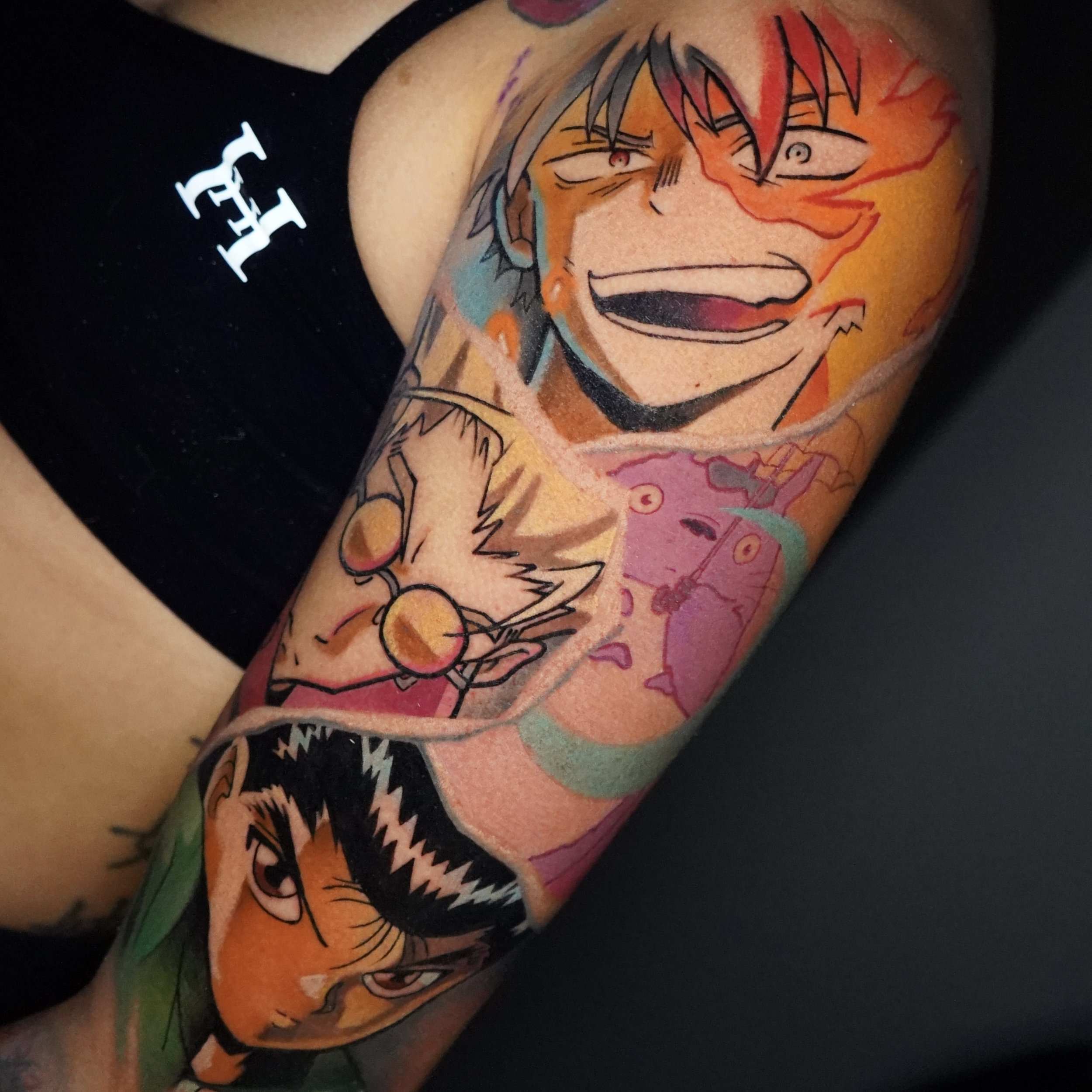 Colorful tattoo sleeve featuring multiple anime characters, including a smiling character with intense eyes, a character with glasses, an angry character with black hair, and another with red hair, all in a vibrant, energetic style.