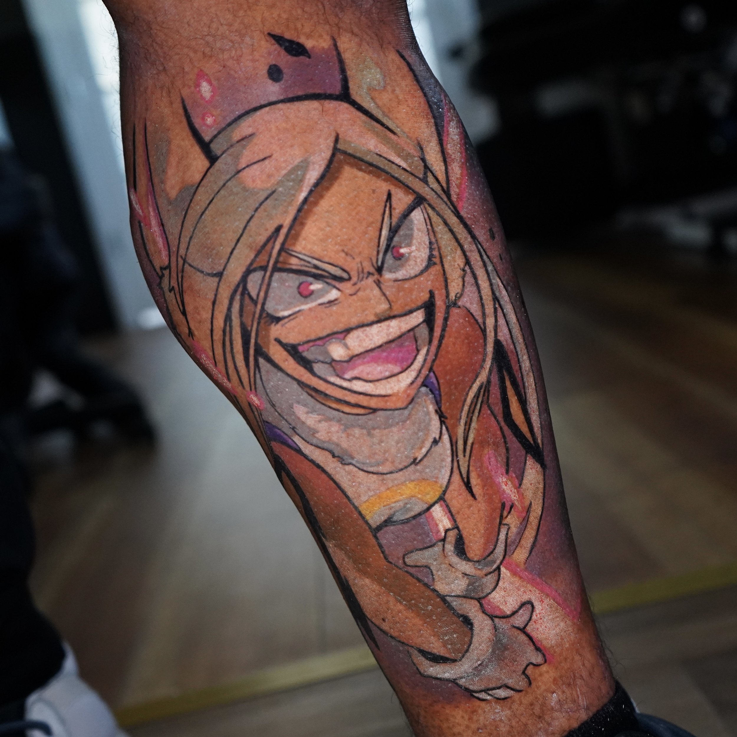 Colorful tattoo of a cartoon character with long hair, horns, and a mischievous expression on the arm.