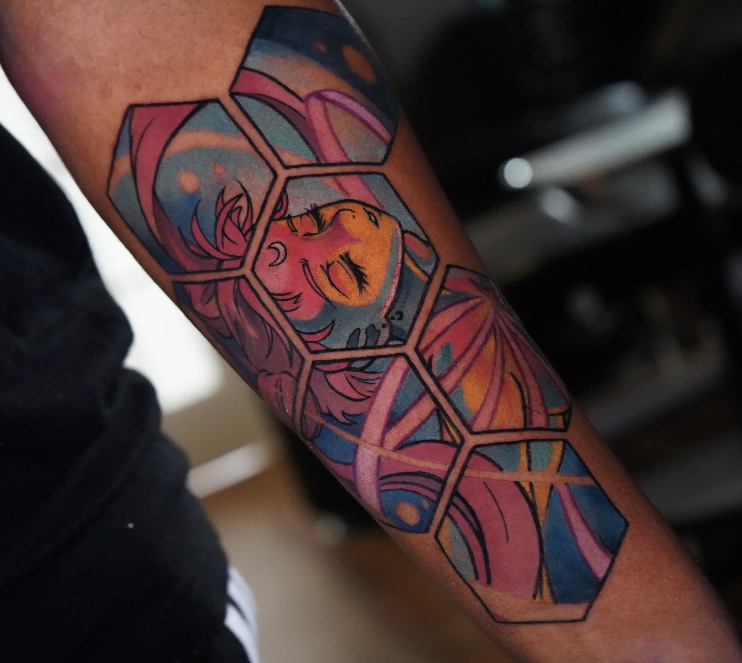 Colorful tattoo of a smiling girl with closed eyes, framed by hexagon shapes, on a person's arm.