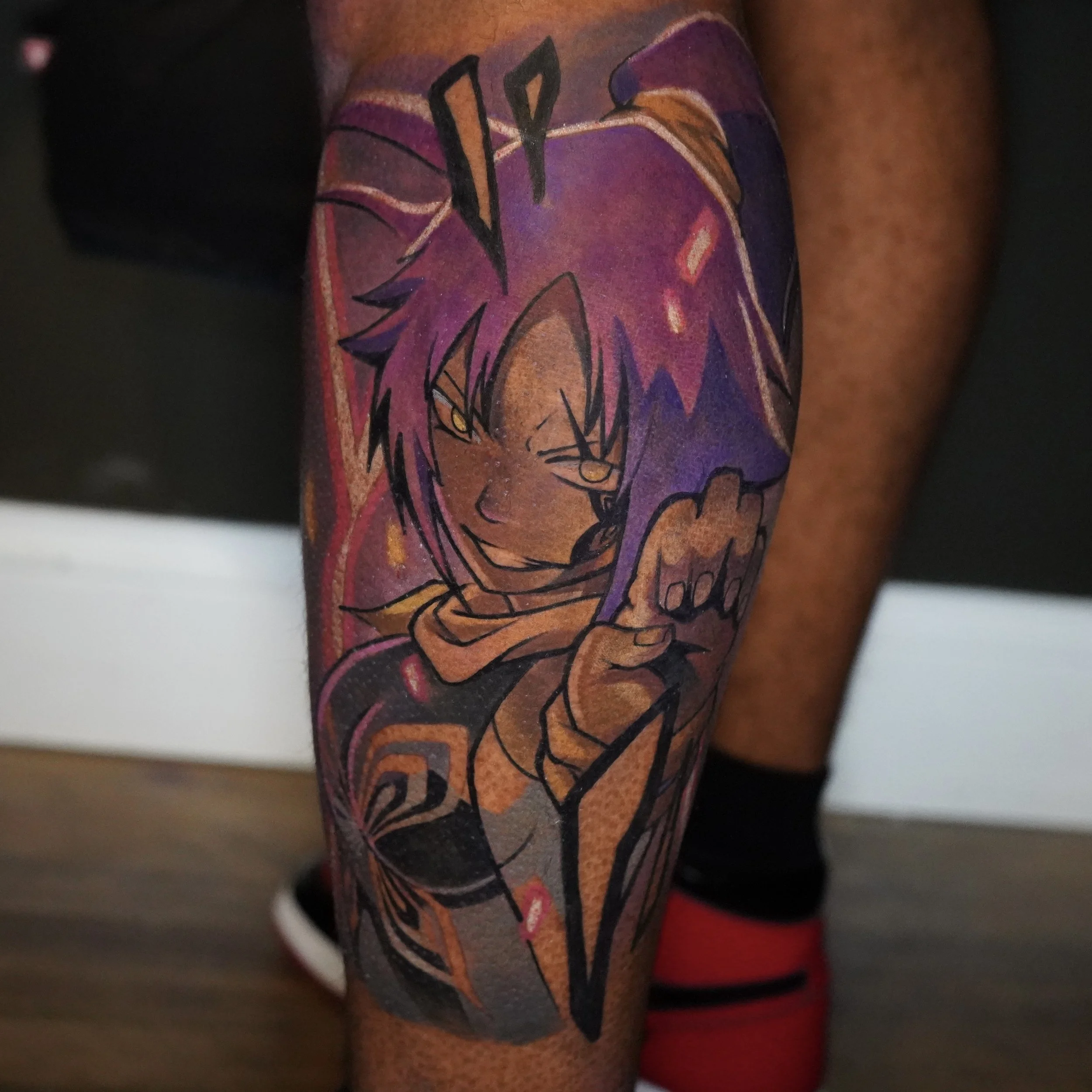 Colorful tattoo of an anime character with spiky purple hair, yellow eyes, and a mischievous expression, on a person's calf.