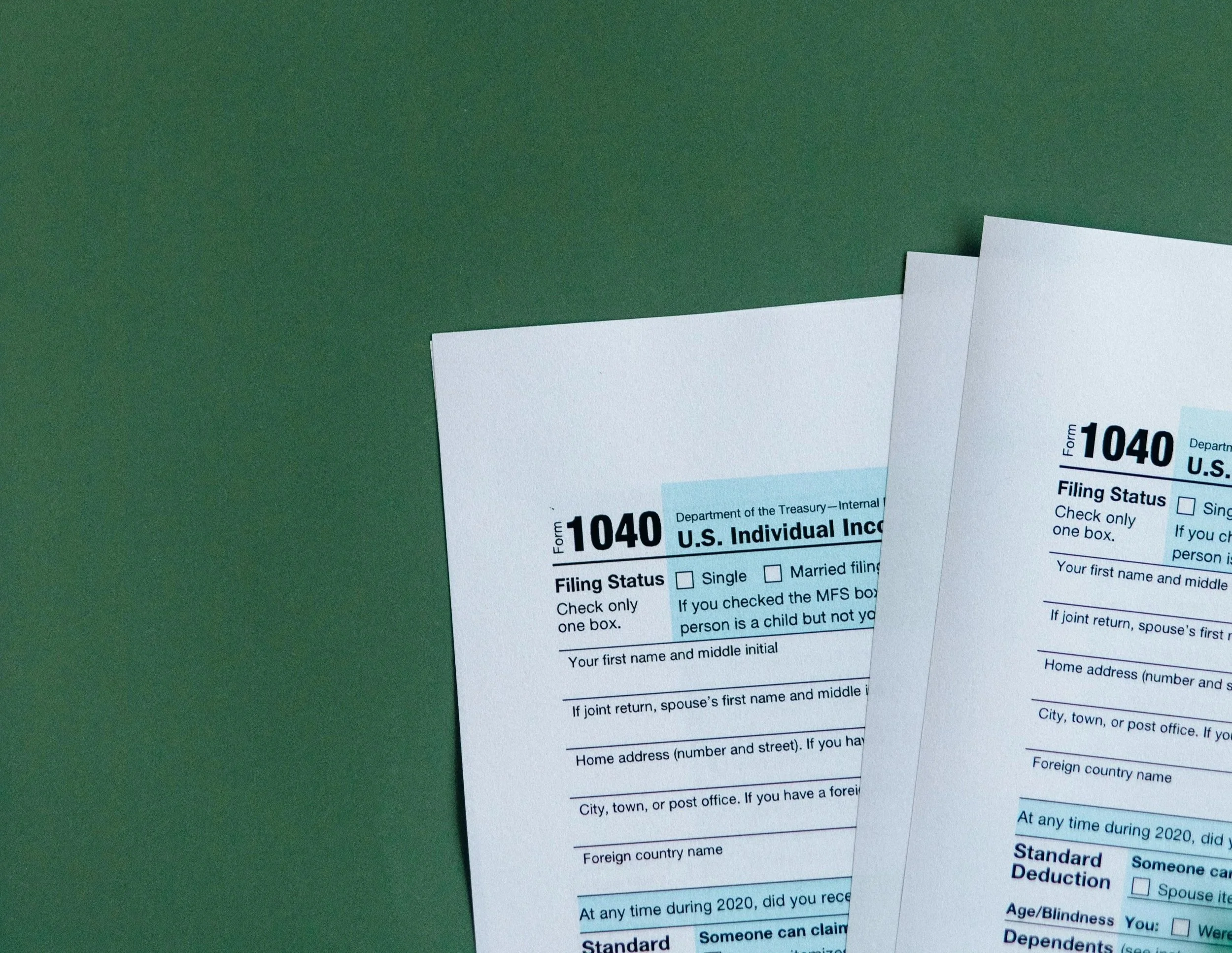 Two U.S. tax forms (1040) placed on a green surface.