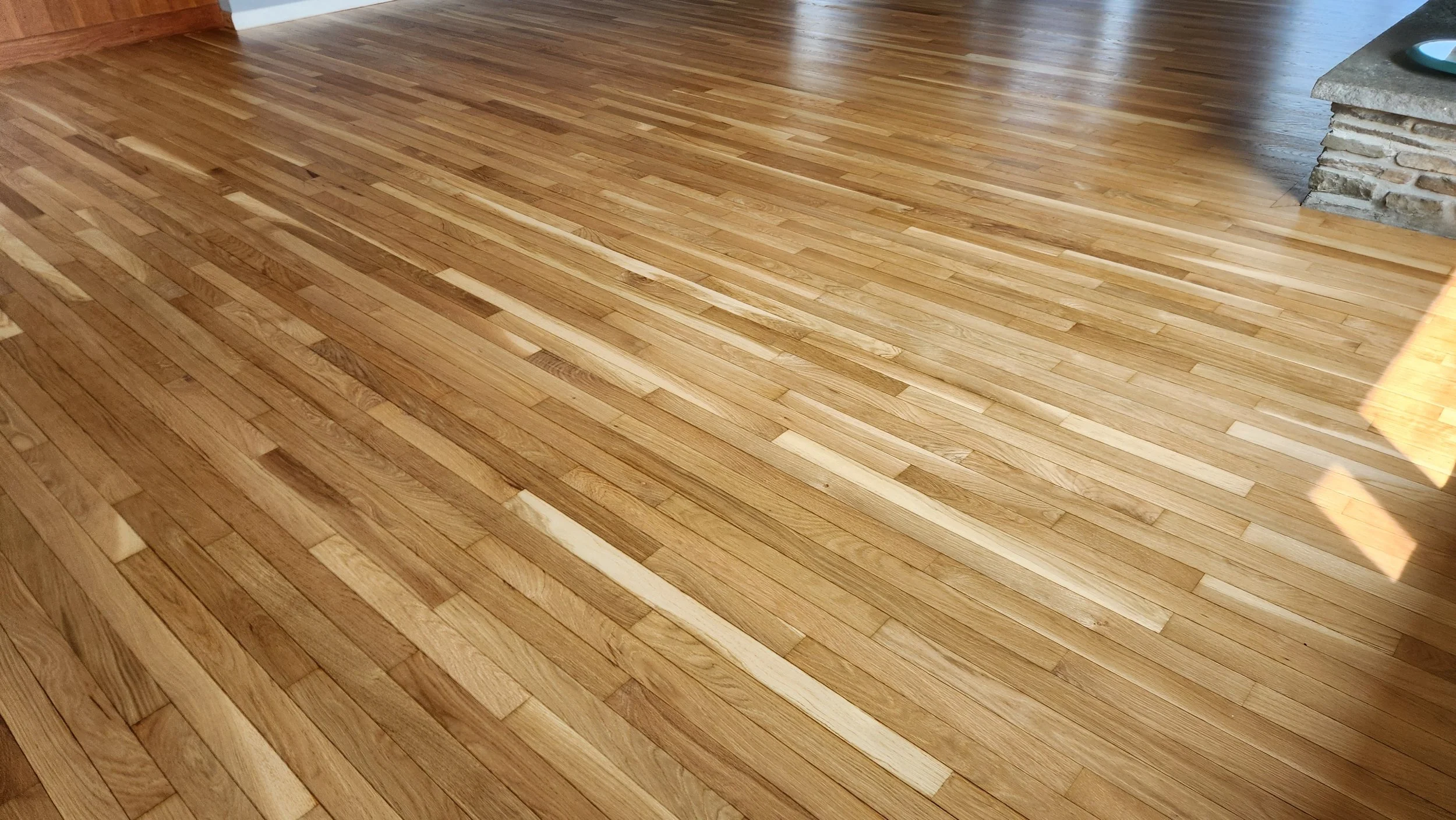 Wooden floor with sunlight reflections and a stone fireplace corner.