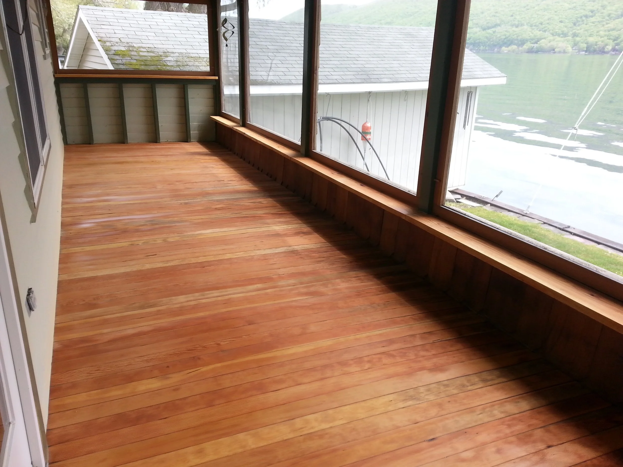 Empty screened porch with wooden floor overlooking a lake.