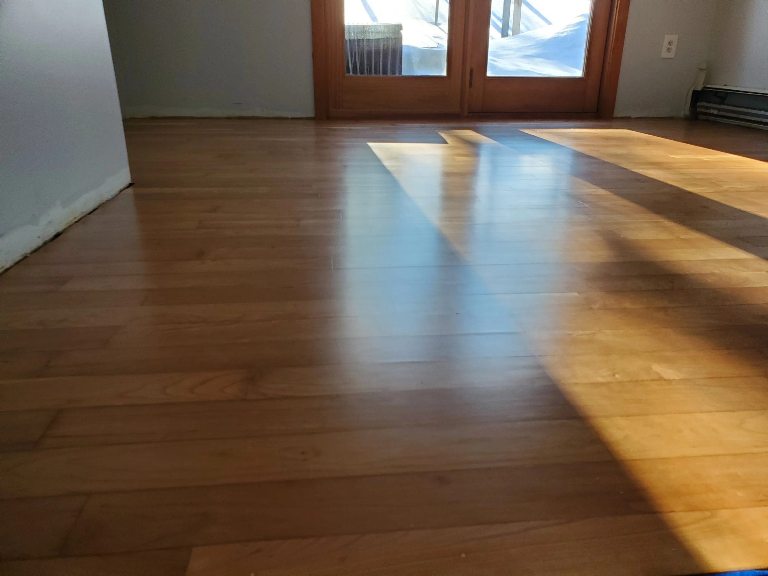 Wooden floor with sunlight casting shadows near a glass door leading outside.