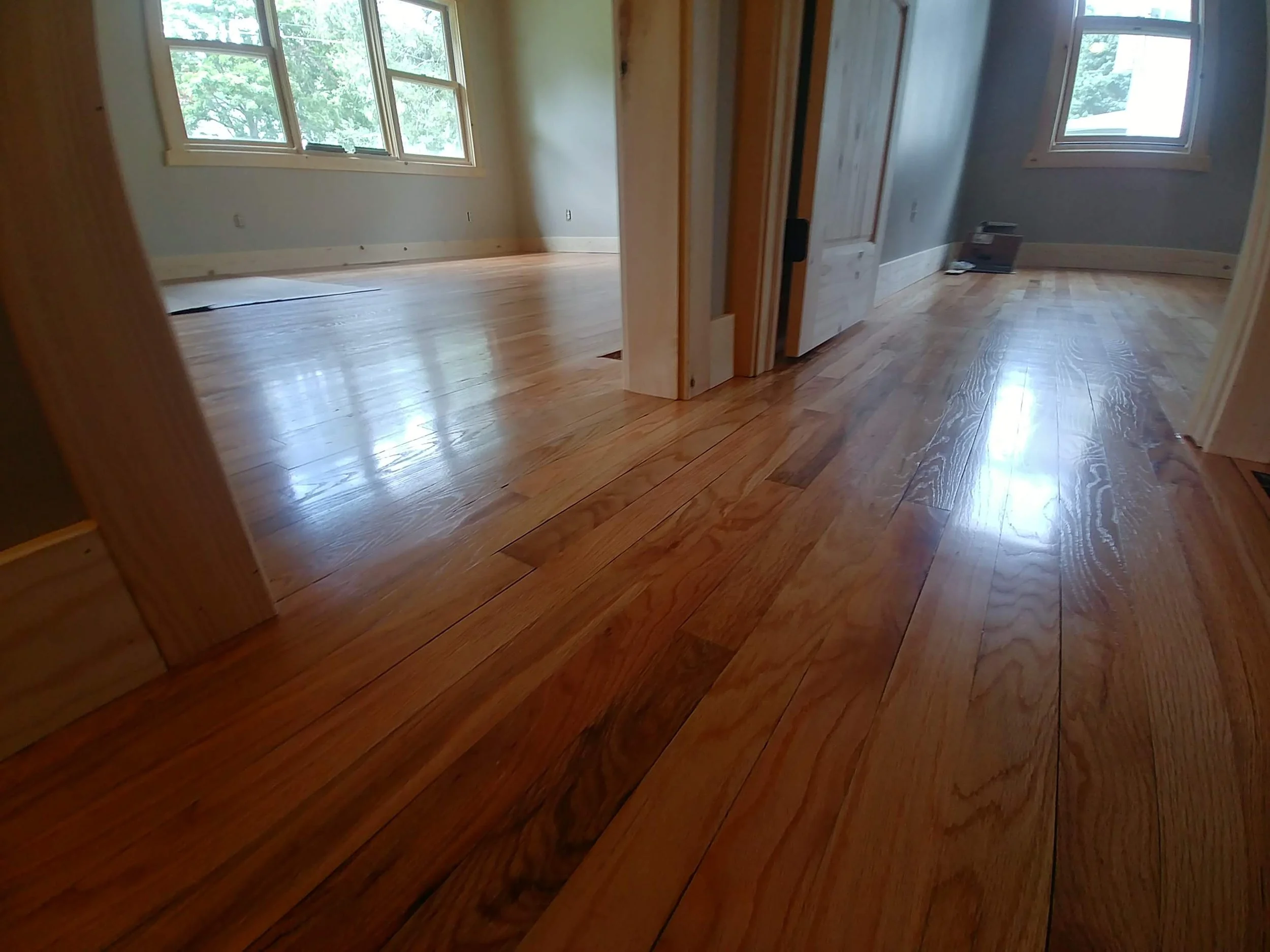 Interior view of a room with polished hardwood floors, large windows letting in natural light, and light-colored walls.