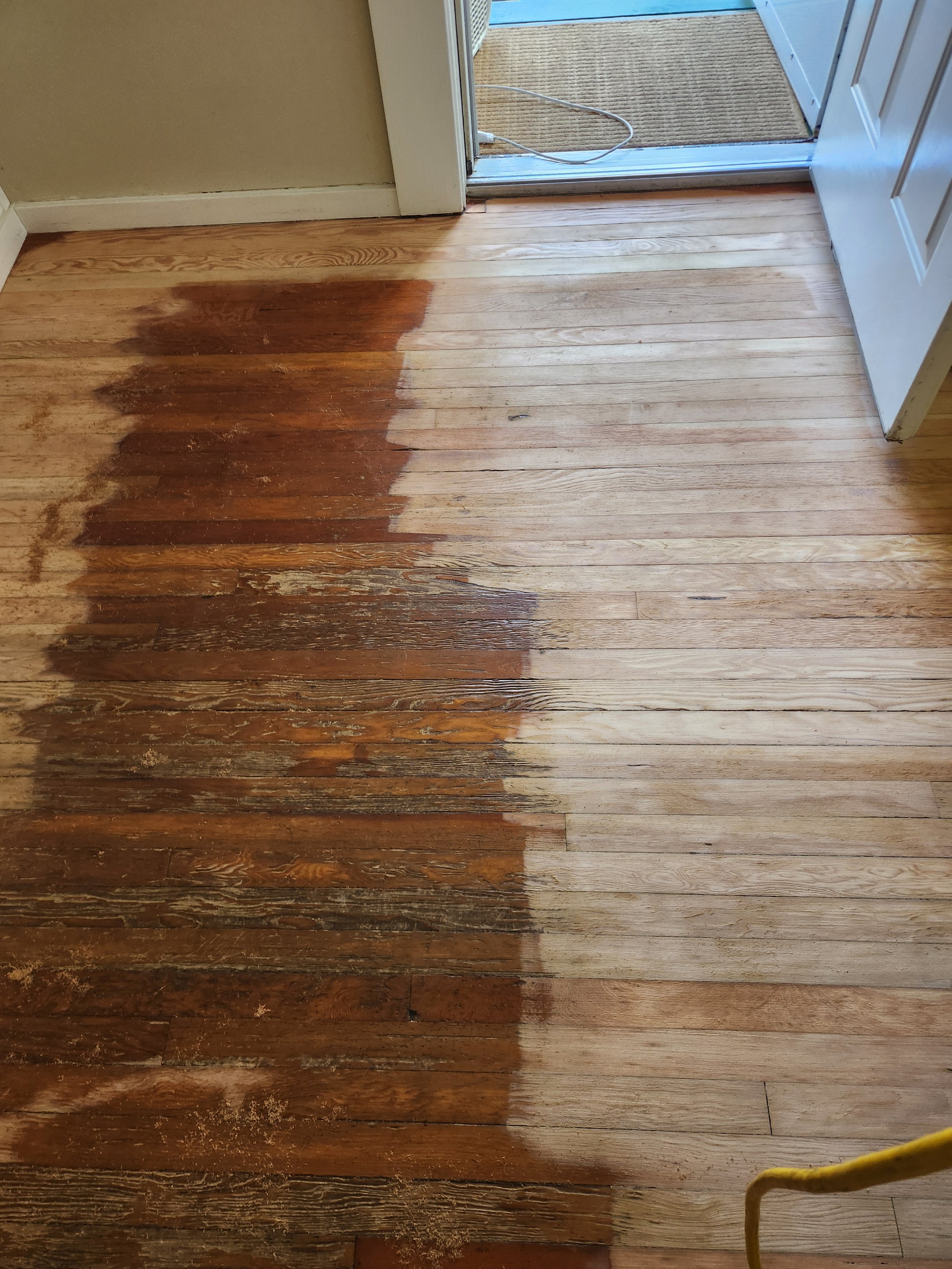 A wooden floor where half of it has been stripped of its old finish and is in the process of being refinished, with the other half still showing the old worn finish.