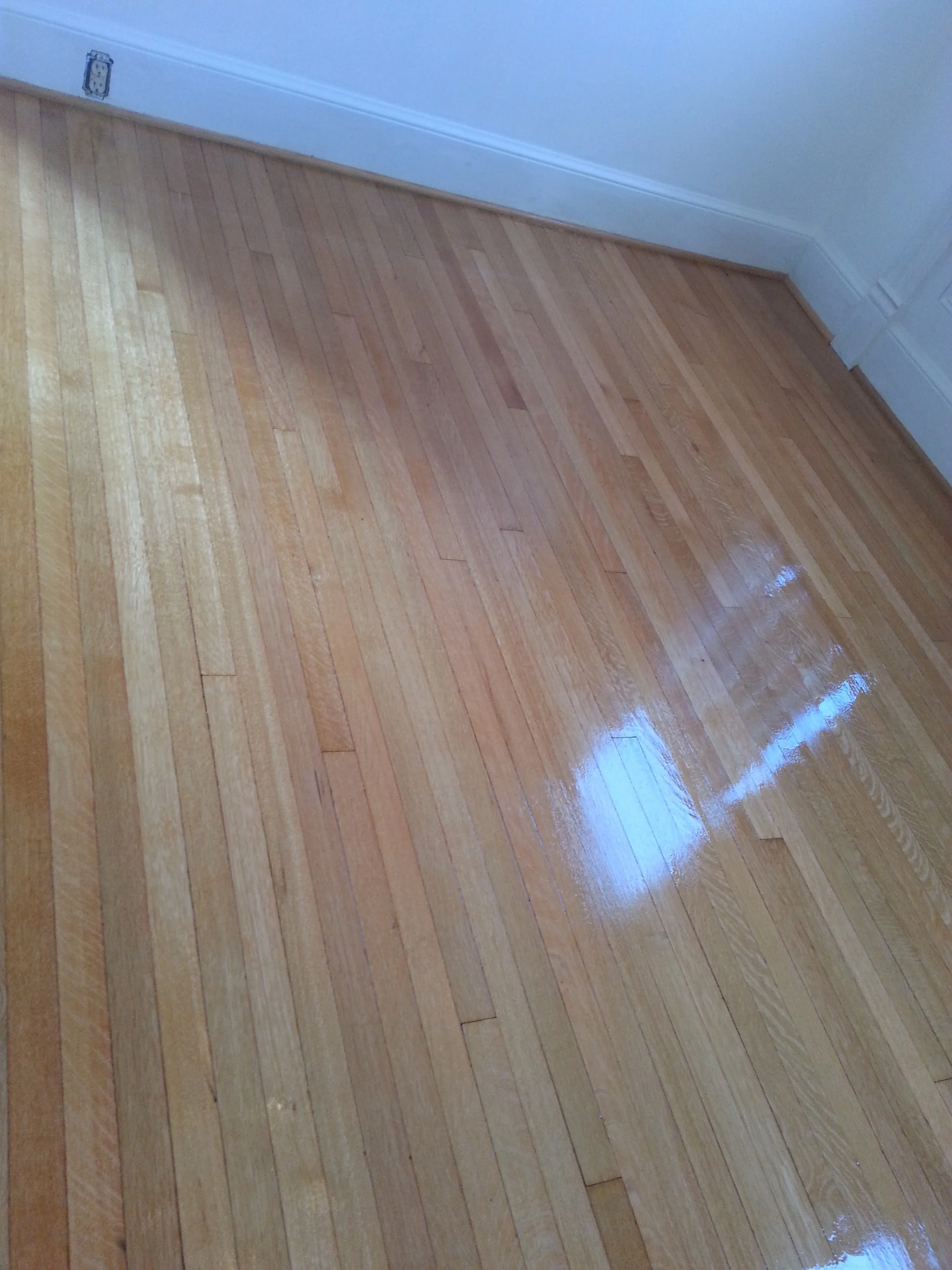 Shiny hardwood floor with a reflection of a window.