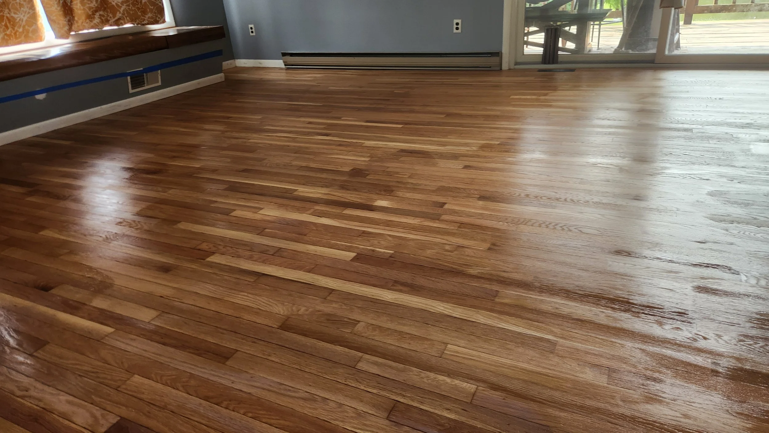 Finished hardwood floor with a shiny, polished surface in a room with large sliding glass doors and a window seat.