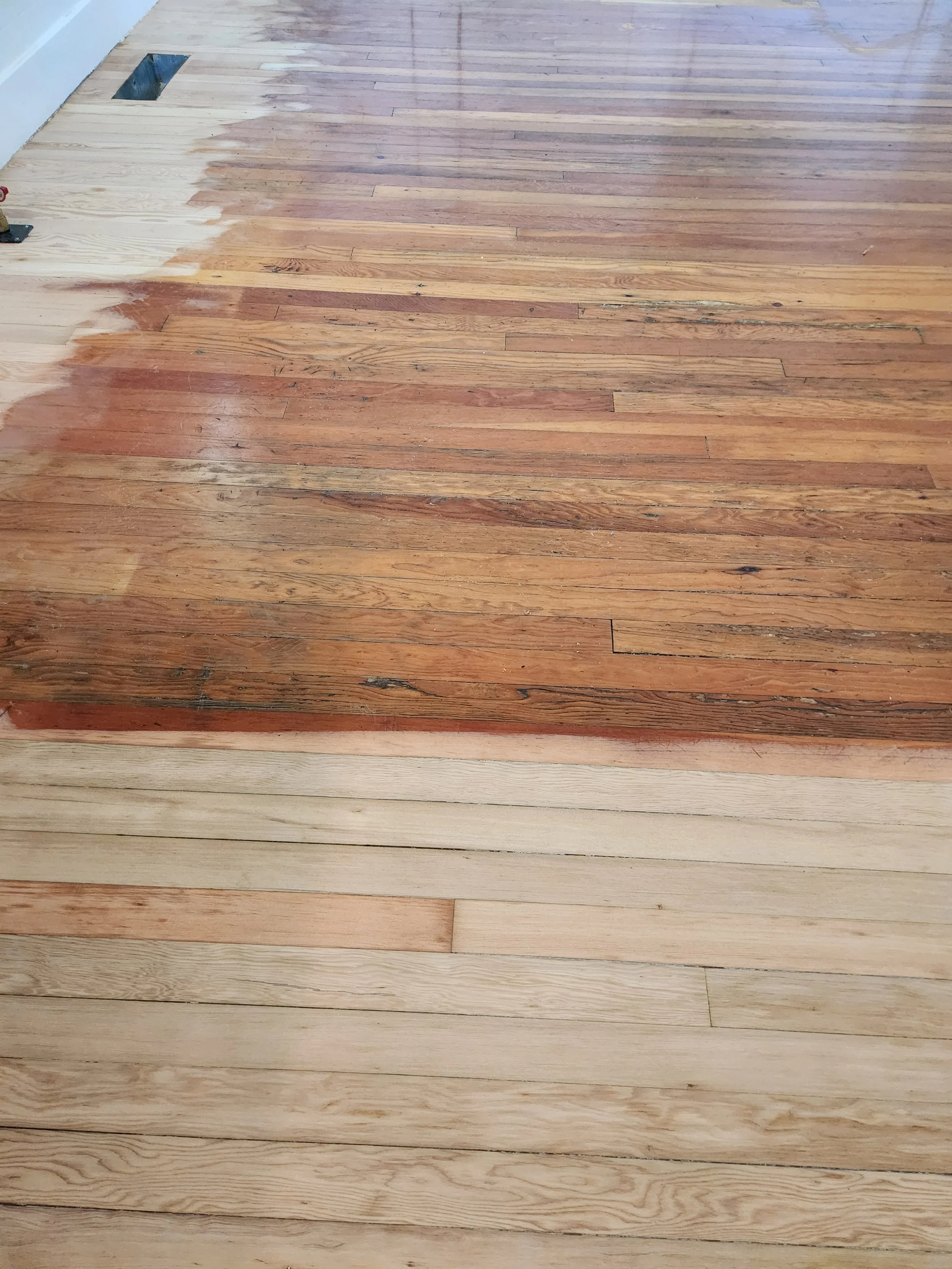 Photo of a wooden floor in the process of being refinished, with the top part showing a darker, older finish and the bottom part showing a lighter, freshly sanded or finished wood.