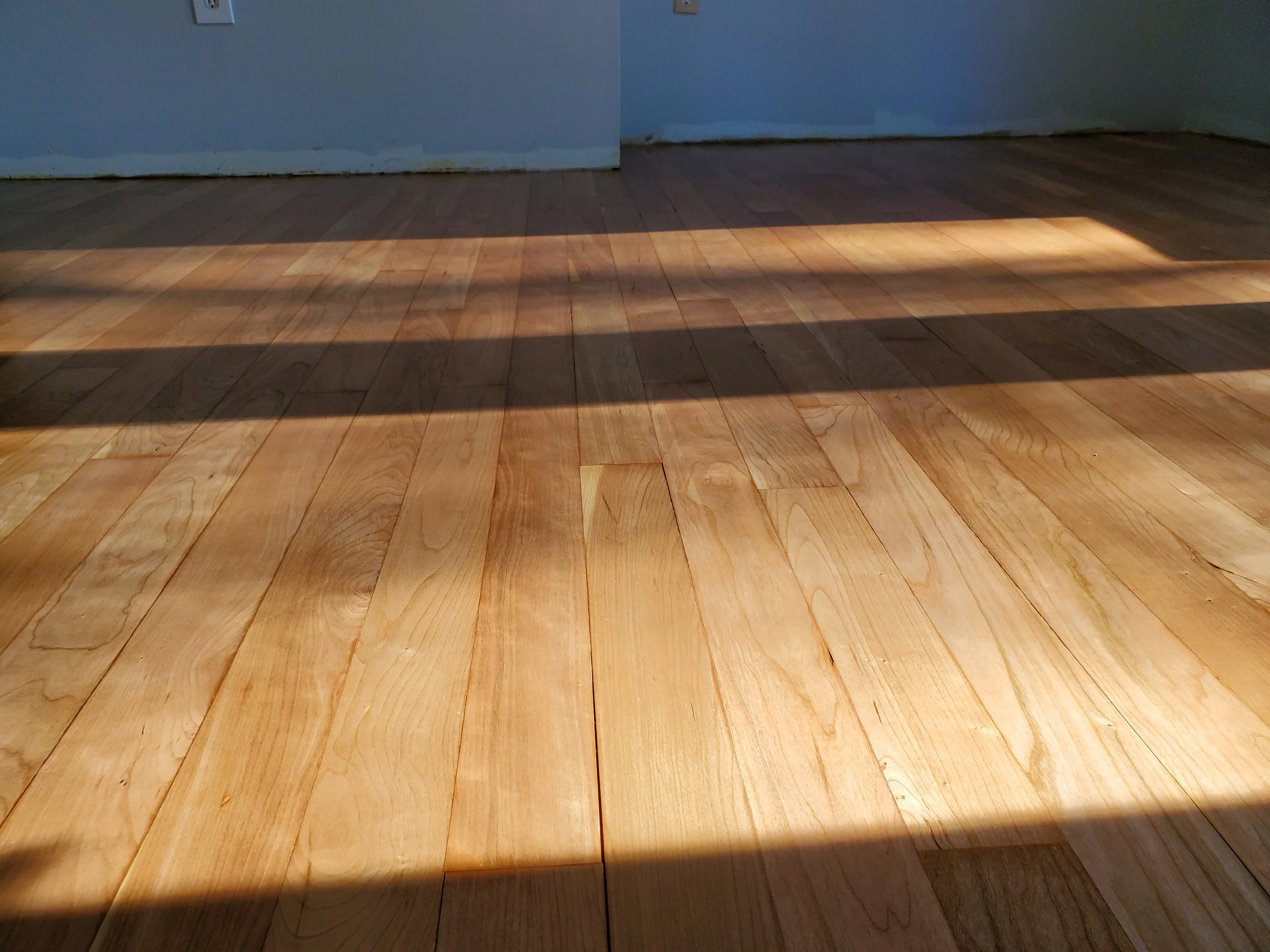 Sunlight casts a rectangular shadow on a wooden floor inside a room.