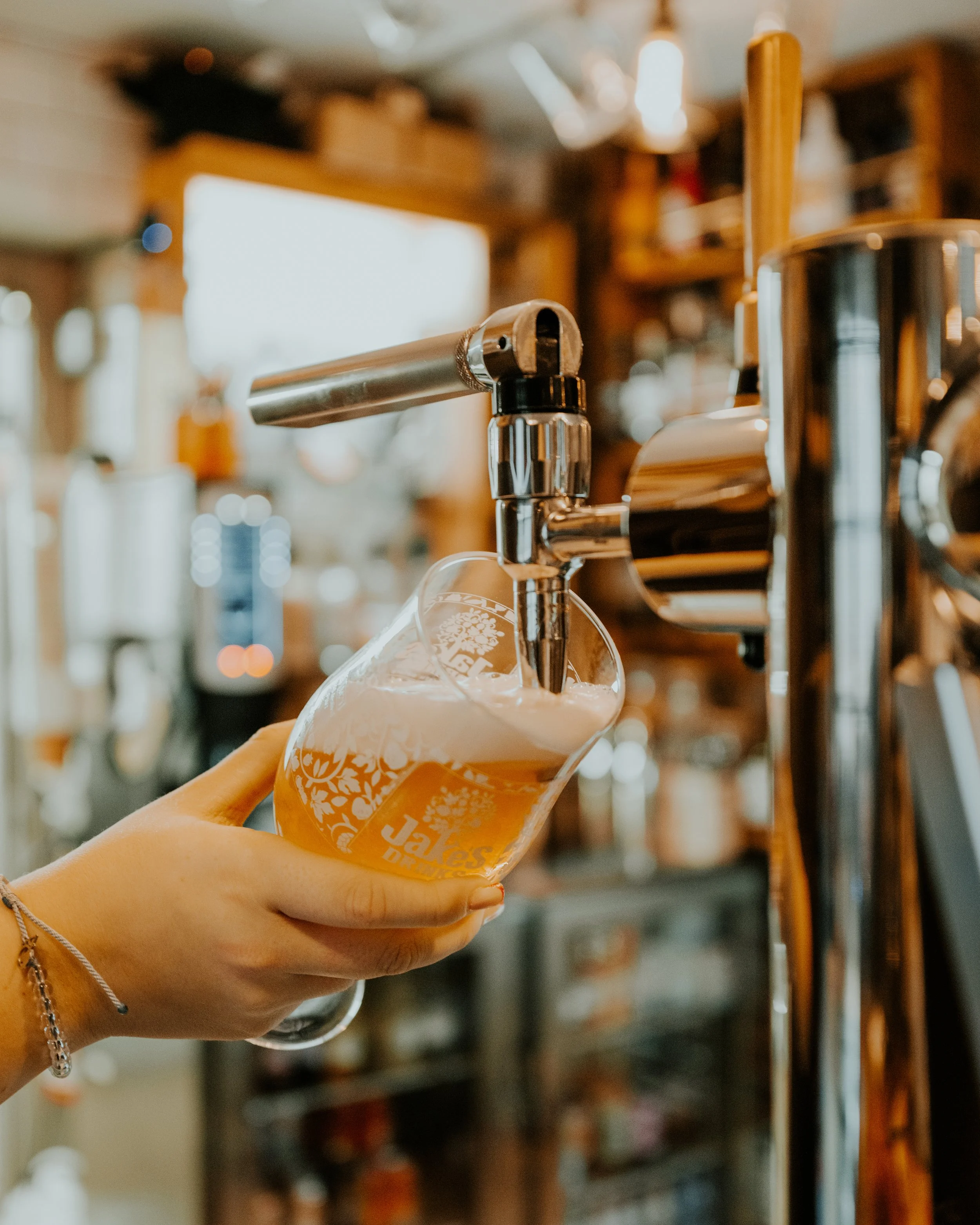 A hand holding a glass under a beer tap pouring beer in a bar or brewery setting.